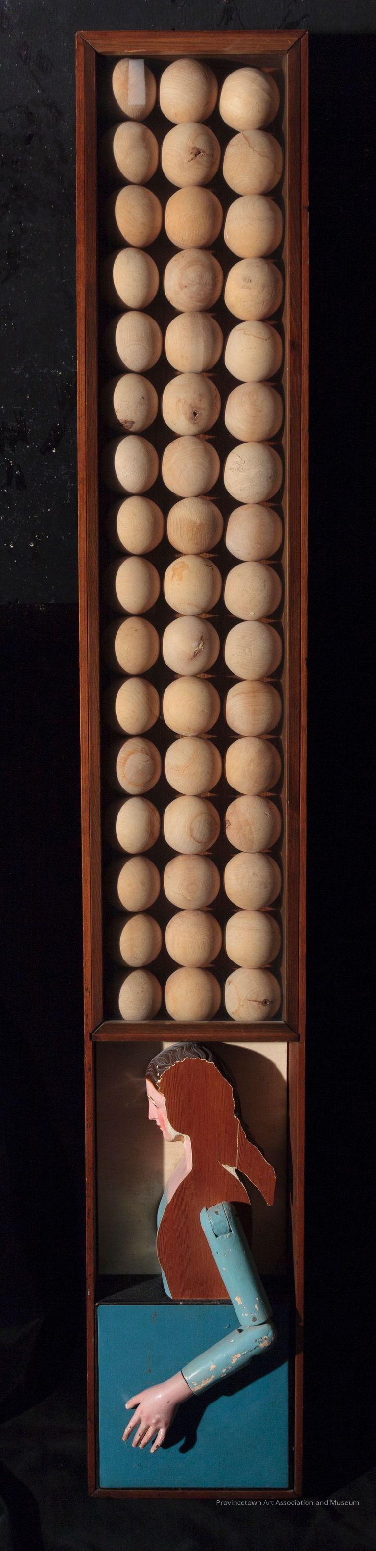 Assemblage of 48 wooden balls arranged in vertical grid, wooden sculpture of female in profile below, all encased in wooden box