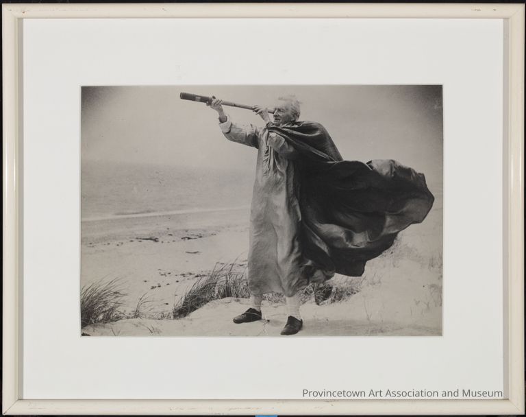 A Harry Kemp, 74 year old, white haired man stands atop the sand dunes. With a telescope in hand, he investigates the oceans waves beyond. The wind whip his cloak mimicking the bend of the sea grass bordering the dunes plateau.