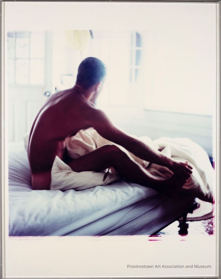 Back profile view of a man sitting upright in bed and looking out the window