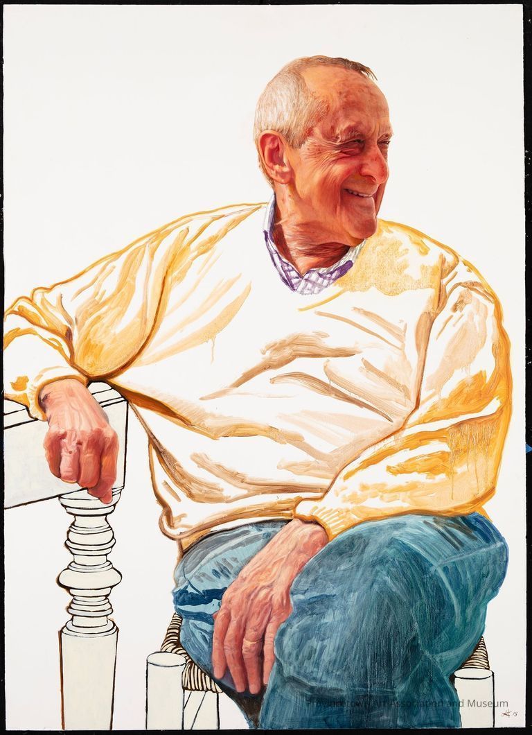 Portrait of the artist Andre Gregory in yellow sweater and jeans, sitting at a table, looking off smiling