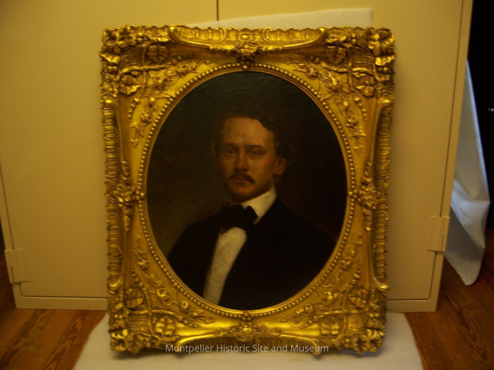 Painting--Richard Snowden Contee: The image depicts an ornate and elaborately designed golden frame surrounding a classical portrait painting. The frame is richly detailed with floral and decorative motifs, emphasizing elegance and grandeur. Within the frame, there is a painting of Richard Snowden Contee in formal attire, wearing a dark suit and a crisp white shirt, along with a neatly tied bow tie. His expression is serious and contemplative, with a well-groomed mustache and styled hair.
Description generated by AI with edits by Museum staff.
