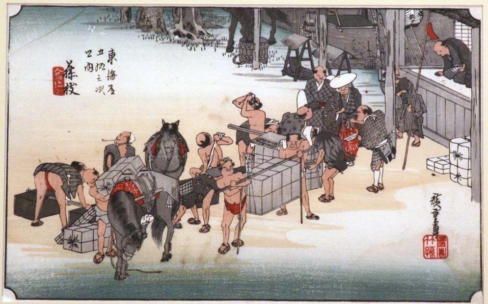 In this traditional Japanese artwork, a busy scene unfolds with people, some carrying heavy loads, interacting with vendors at a riverside market. Horses are laden with goods, highlighting the importance of trade. The detailed, colorful attire contrasts with the calm expressions of the figures, capturing a glimpse of daily life in Japan long ago.