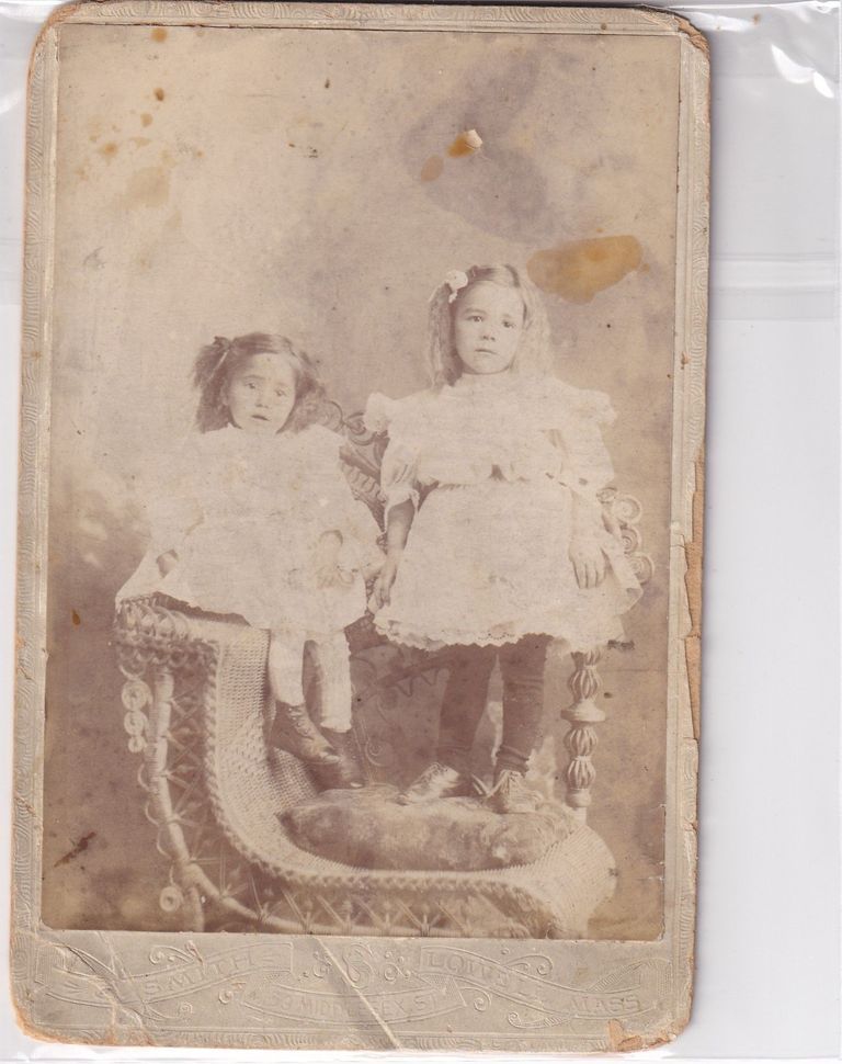 Portrait of Two Young Girls Seated on Wicker Studio Chair with Fur Throw