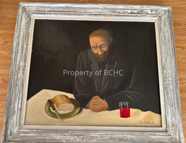 Man sitting at a table praying with a loaf of bread and a drink.