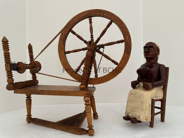 Three piece carving depicting  a woman sitting at a spinning wheel.