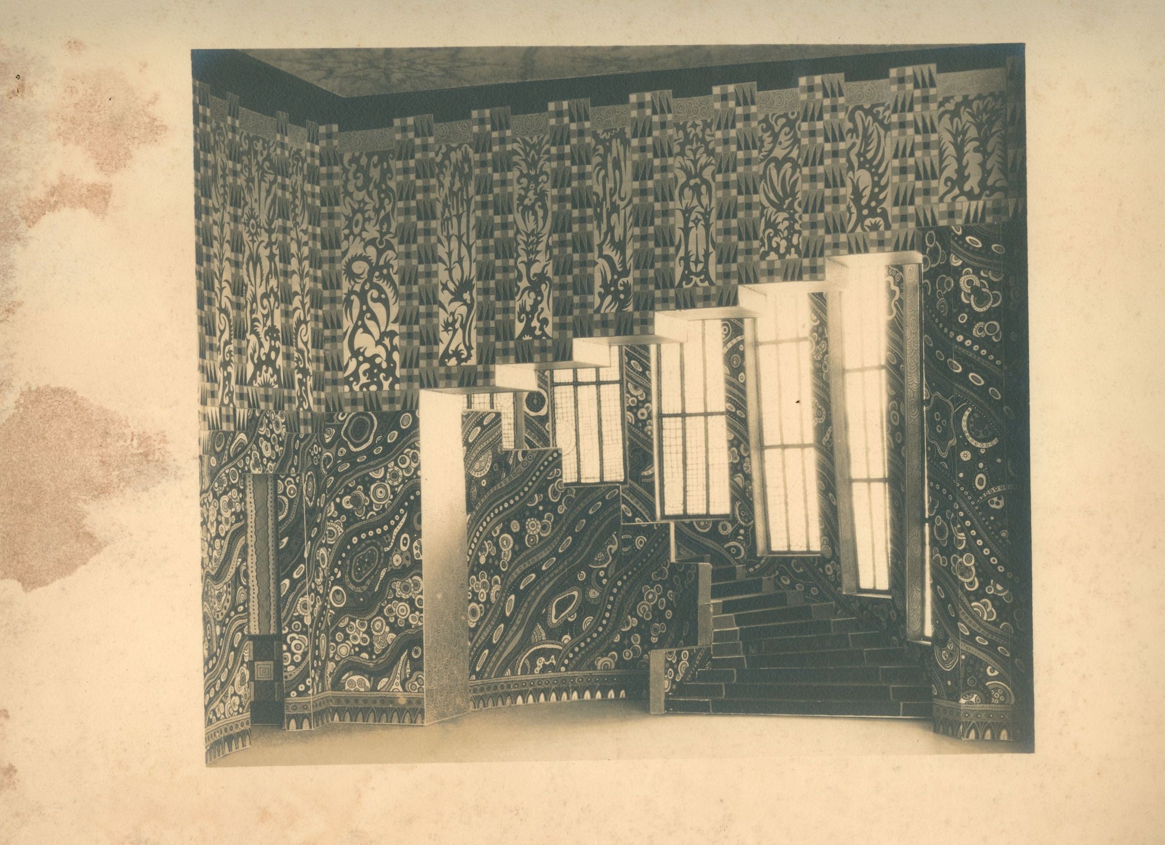 The artwork by John Hawkins features an architectural collage that intricately blends patterns, textures, and geometric forms, creating an abstract representation of an interior space with layered walls and staircases adorned in elaborate, swirling paisley and floral designs, alongside checkered borders, while the shadows cast by imagined windows add depth and dimension, evoking a sense of surrealism and complexity within a confined space, inviting viewers to explore the interplay between traditional motifs and modern abstraction in its imaginative, almost dreamlike atmosphere.