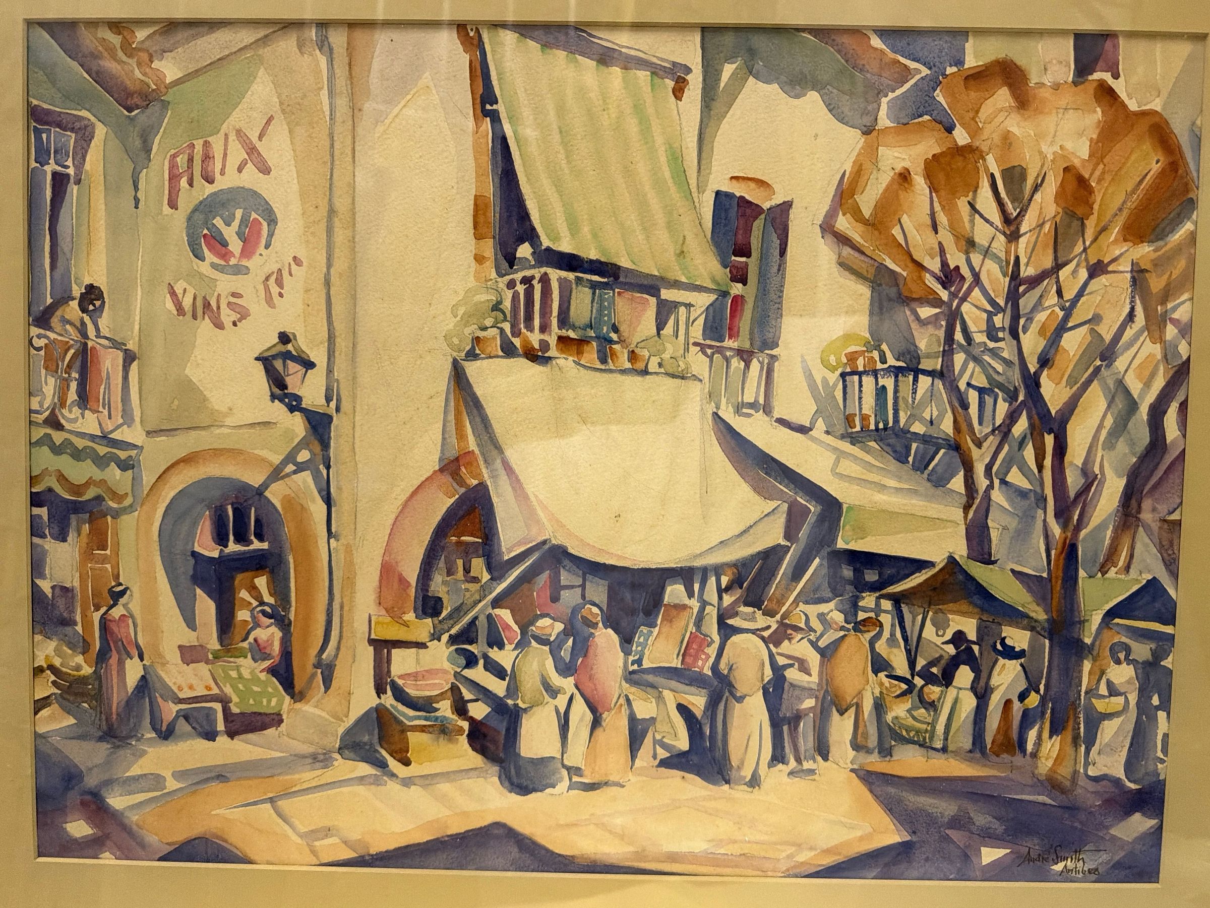 In this lively watercolor, André Smith captures a crowded outdoor market in Antibes, France, where shoppers gather beneath sunlit awnings in the town's narrow streets.: In this watercolor, J. André Smith turns a busy market day in Antibes into a bright mosaic of color and light. Shoppers in hats and long dresses crowd around stalls beneath broad cream and striped green awnings, some carrying baskets, while vendors work from tables set into arched doorways. Above the crowd, balconies spill over with potted plants, and a woman leans from a balcony at left beside a painted wall sign advertising wine ("Vins"). A street lamp juts from the wall on an iron bracket, and at right a tree with warm ochre foliage and bare violet branches rises over the market umbrellas. Smith breaks the buildings, shadows and pavement into angular, faceted planes, a sign of the Cubist influence that also shapes his etchings of the period, while loose washes of ochre, rose, violet and pale green give the scene its warmth and movement. Faint pencil underdrawing remains visible beneath the paint in places. Signed and inscribed "André Smith / Antibes" at lower right, the work is a vivid record of everyday life on the Côte d'Azur and a colorful companion to Smith's prints of the same town.