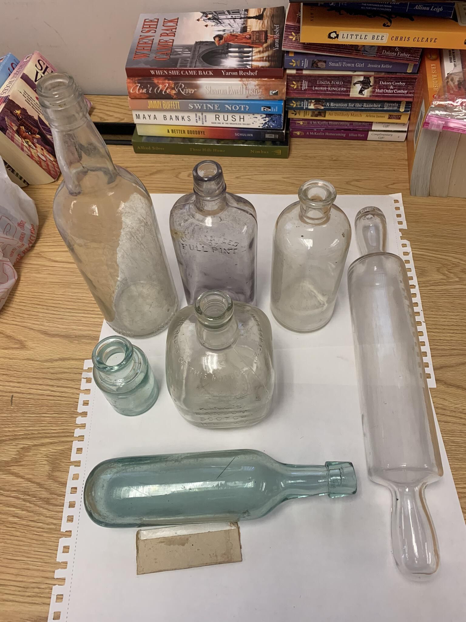 Miscellaneous glass bottles mostly donated by MacMcEvilly: Specifically, from back to front these items include:
- A nondescript quart screw top whiskey bottle (likely $0 value);
- A significantly naturally sun purpled Guaranteed Full Pint whiskey bottle which might bump the value of this otherwise common item to $25 or more (refer to the weblinks section for an explanation of sun purpling);
- A nondescript pint bottle (likely $0 to $5 value);
- A glass rolling pin with a bottle like open end (estimated $65 to $85 vale);
- A nondescript probable ink bottle (likely $0 to $3 value);
- A king's Ransom scotch whiskey bottle (likely $20 to $40 value additional photo follows), and;
- A nondescript round bottom wine or carbonated beverage bottle (likely $10 to $20 value). The rounded bottom ensured side storage to prevent its cork from drying out and failing.