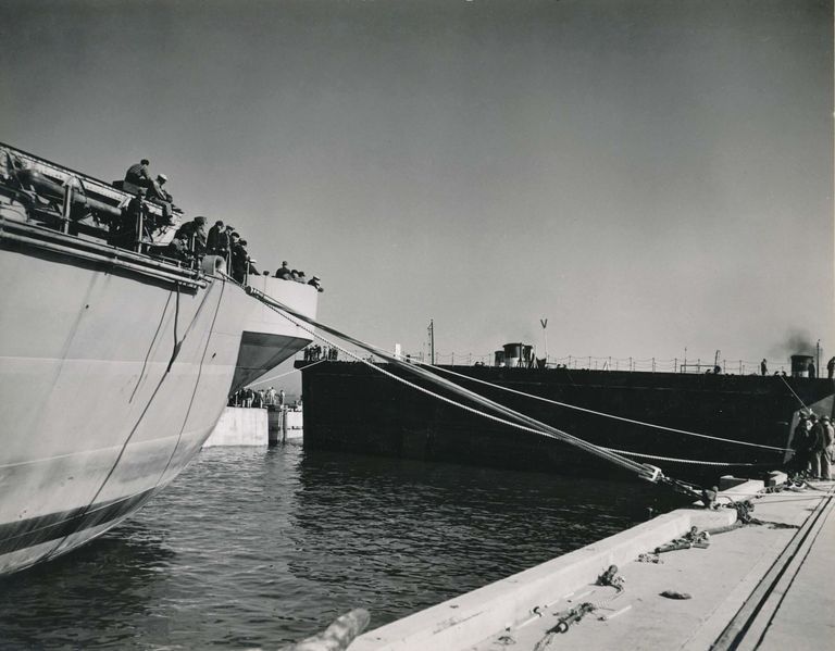          Workers on IOWA's stern continue to adjust the lines as the tug boats push the caisson into its final position. October 20, 1942 - 80-G-13564 picture number 1
   