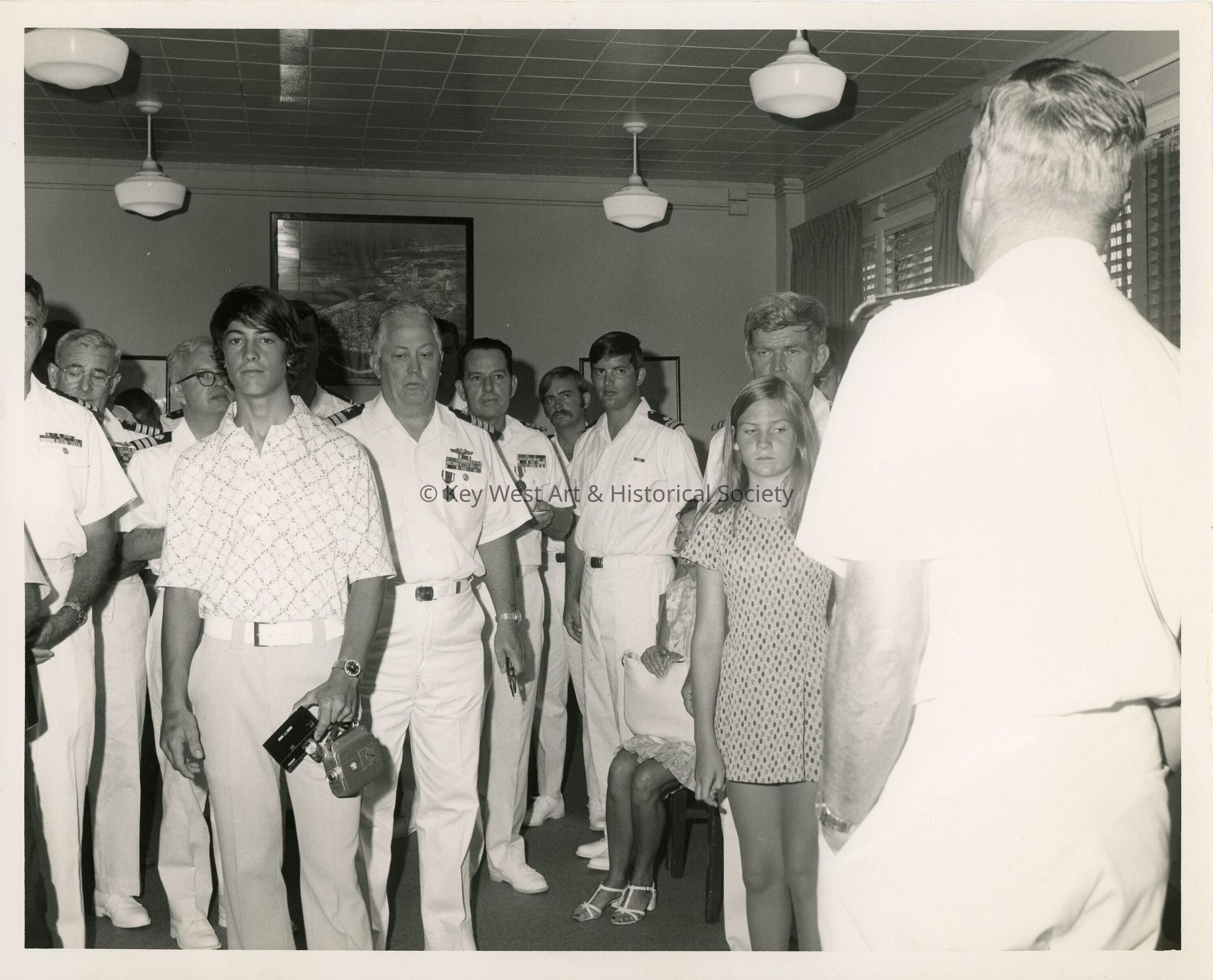 A group of  U.S. Military men with unkown people standing in a room