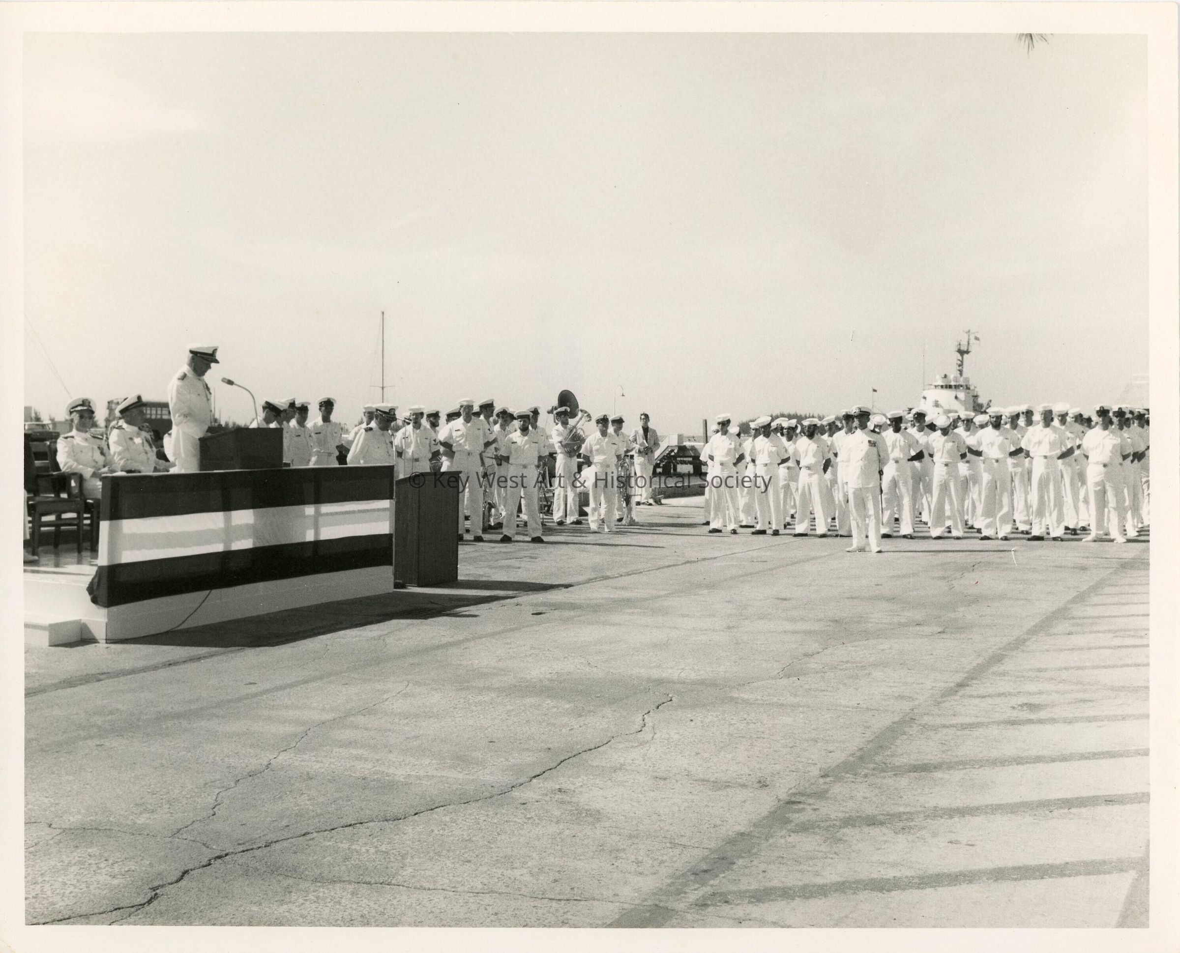 A group of unknown people in uniform standing while one speaks at the podiu