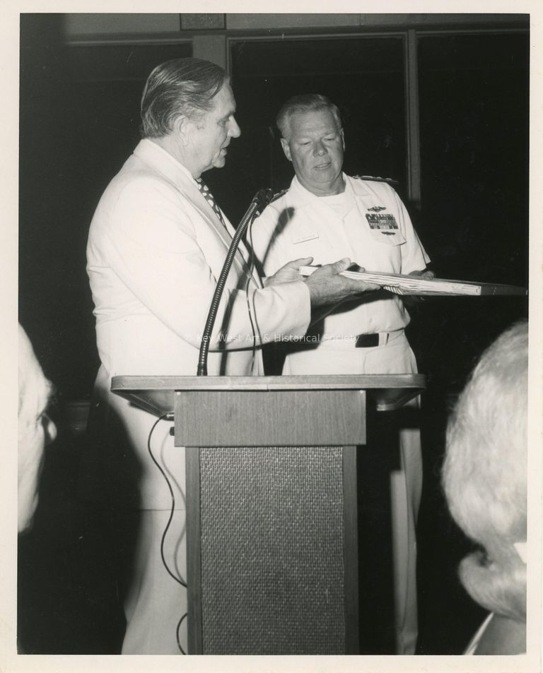 2 Unknown men at a podium, one is receiving an item