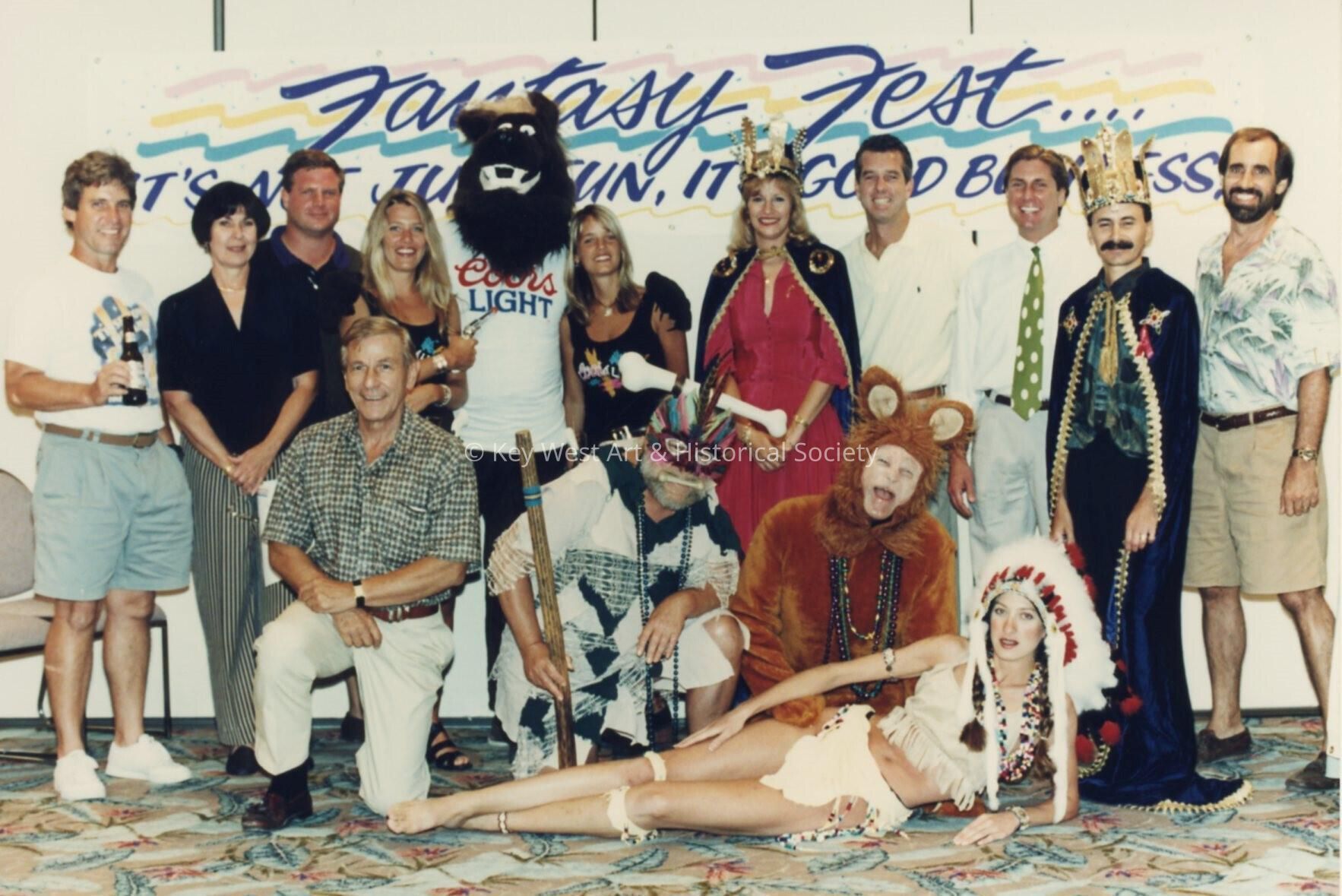 A group of unknown people standing in front of a Fantasy Fest sign.