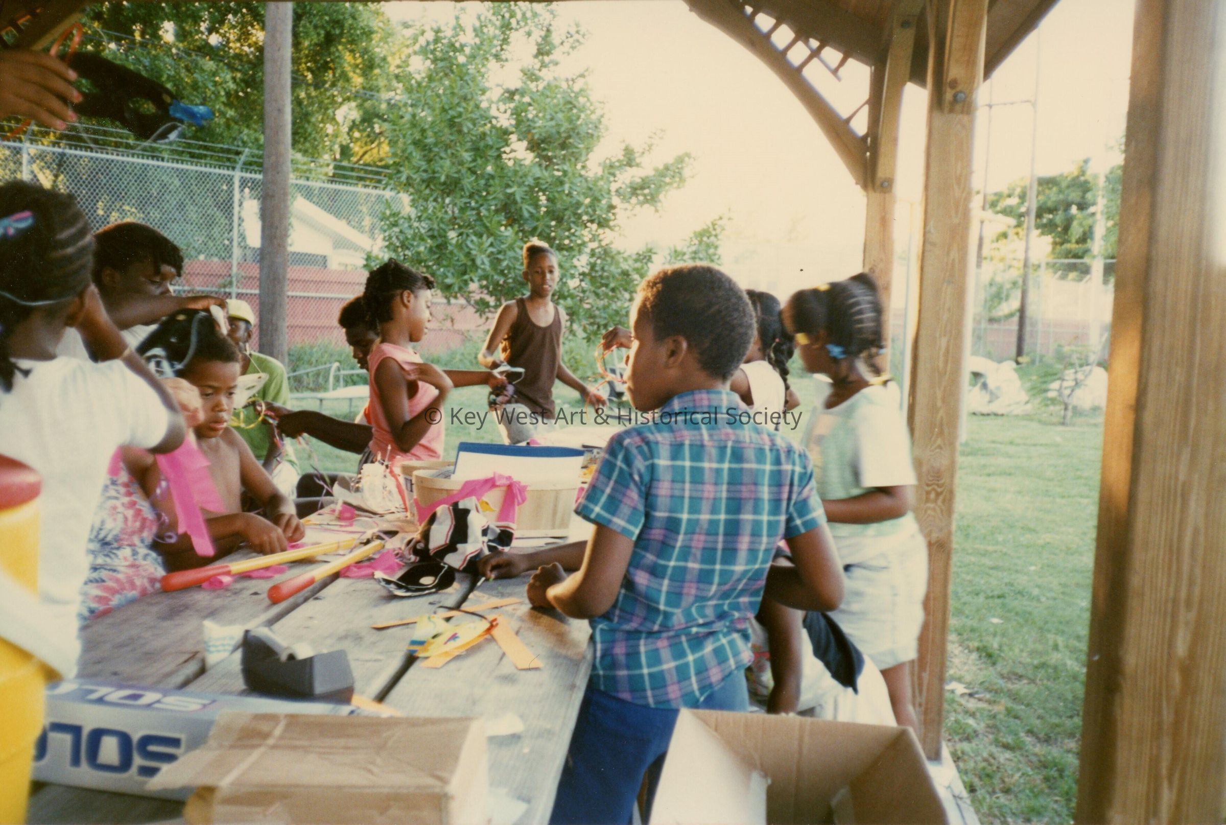 A group of unknown kids working on some crafts at a table outside.