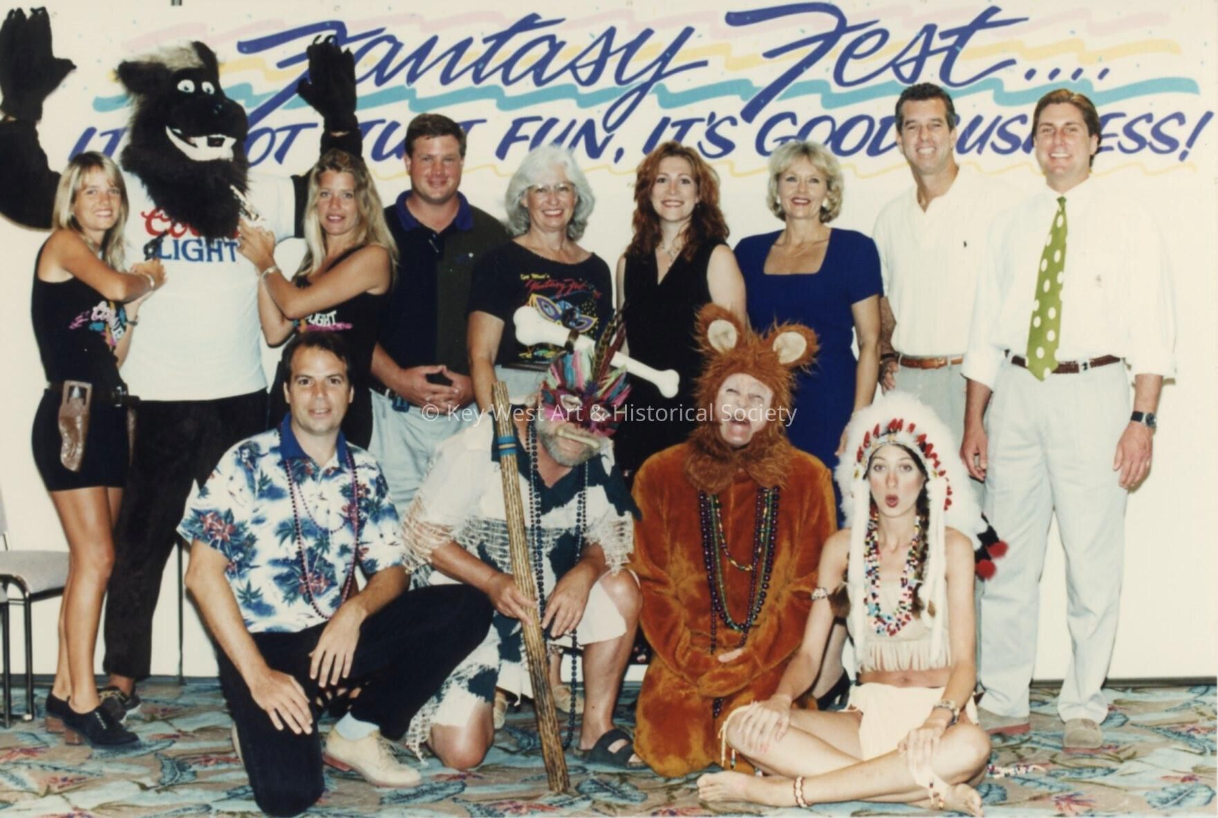A group of unknown people standing in front of a Fantasy Fest sign.