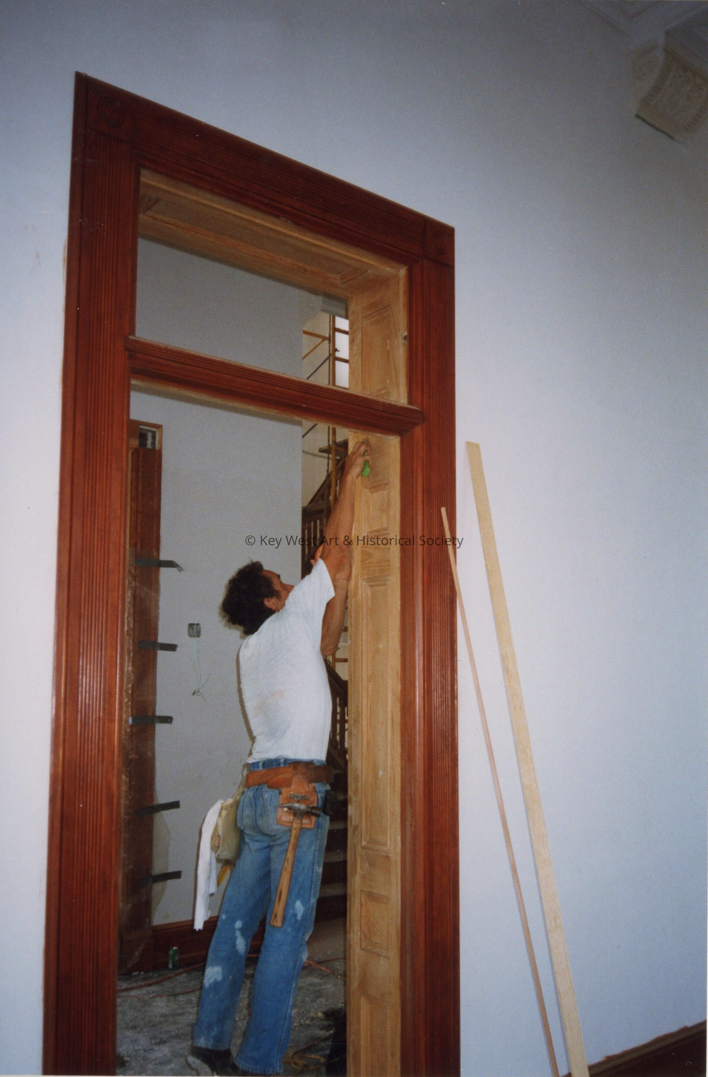 An unknown man working on the wood work on one of the doorways.