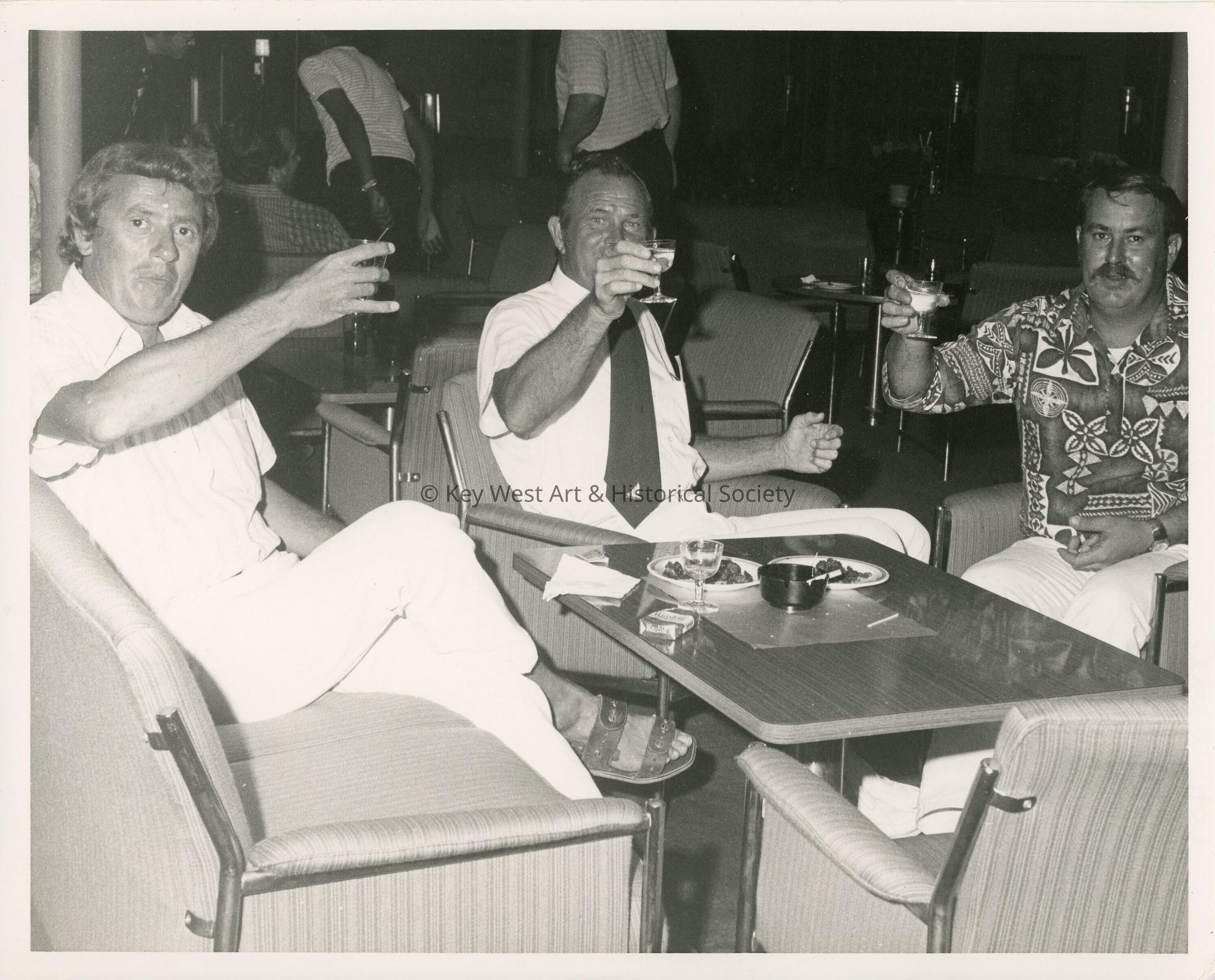 3 Unknown men sitting at a table holding drinks up