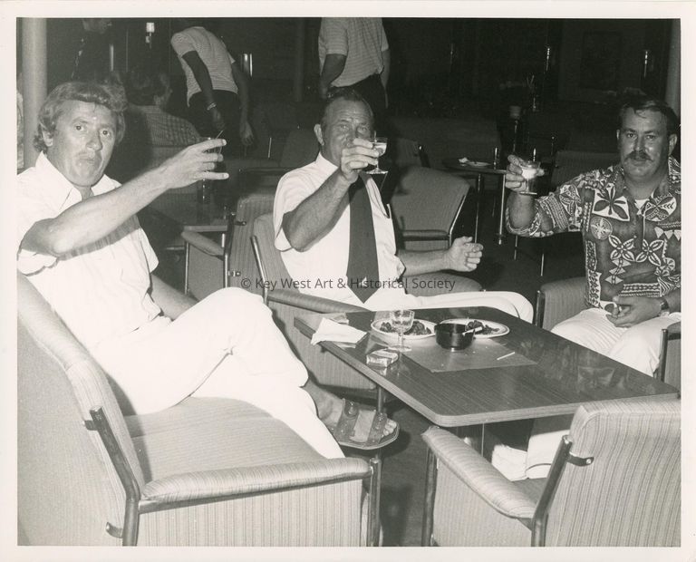 3 Unknown men sitting at a table holding drinks up