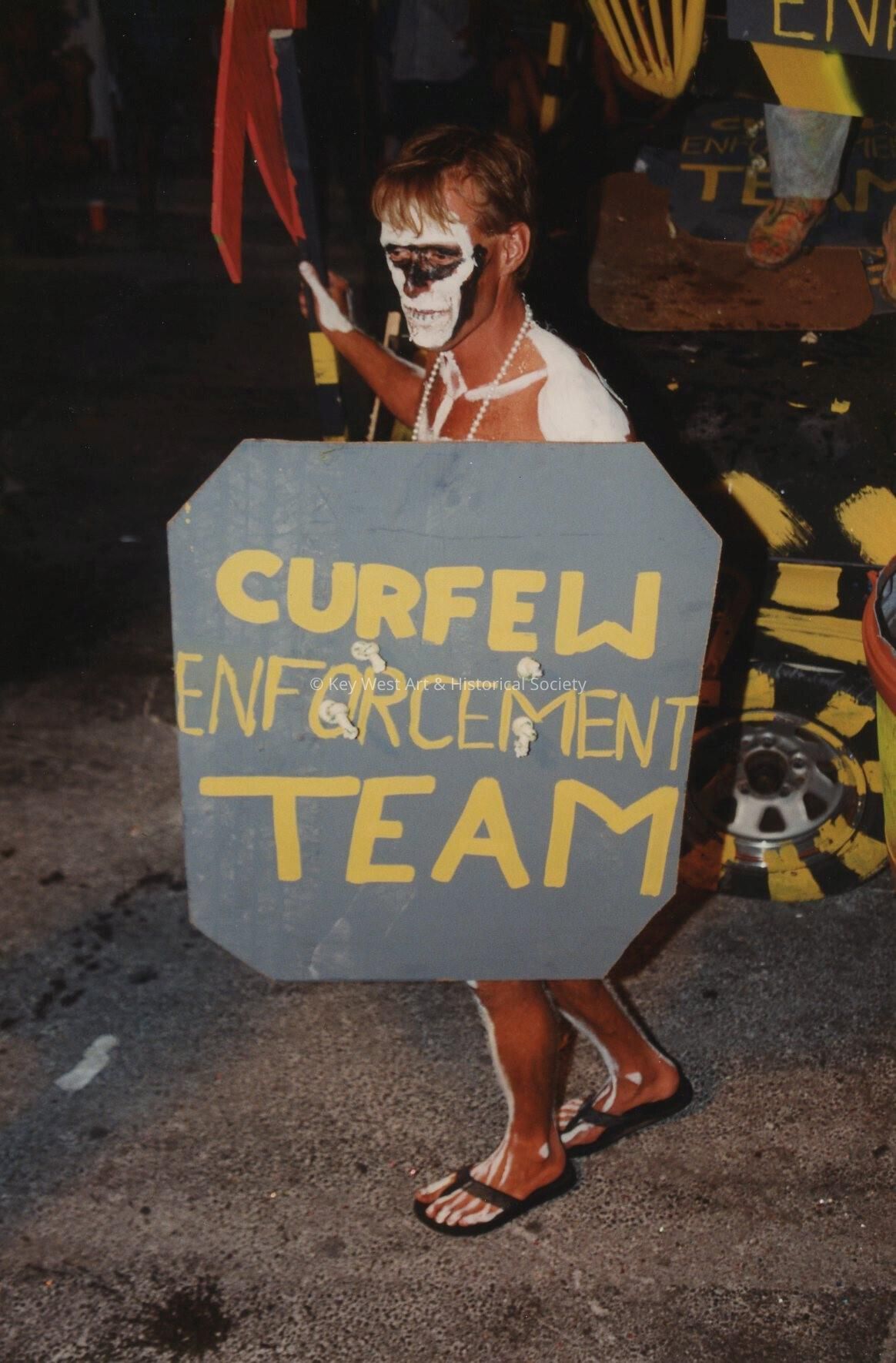 An unknown man dressed up holding a sign that reads curfew enforcement team
