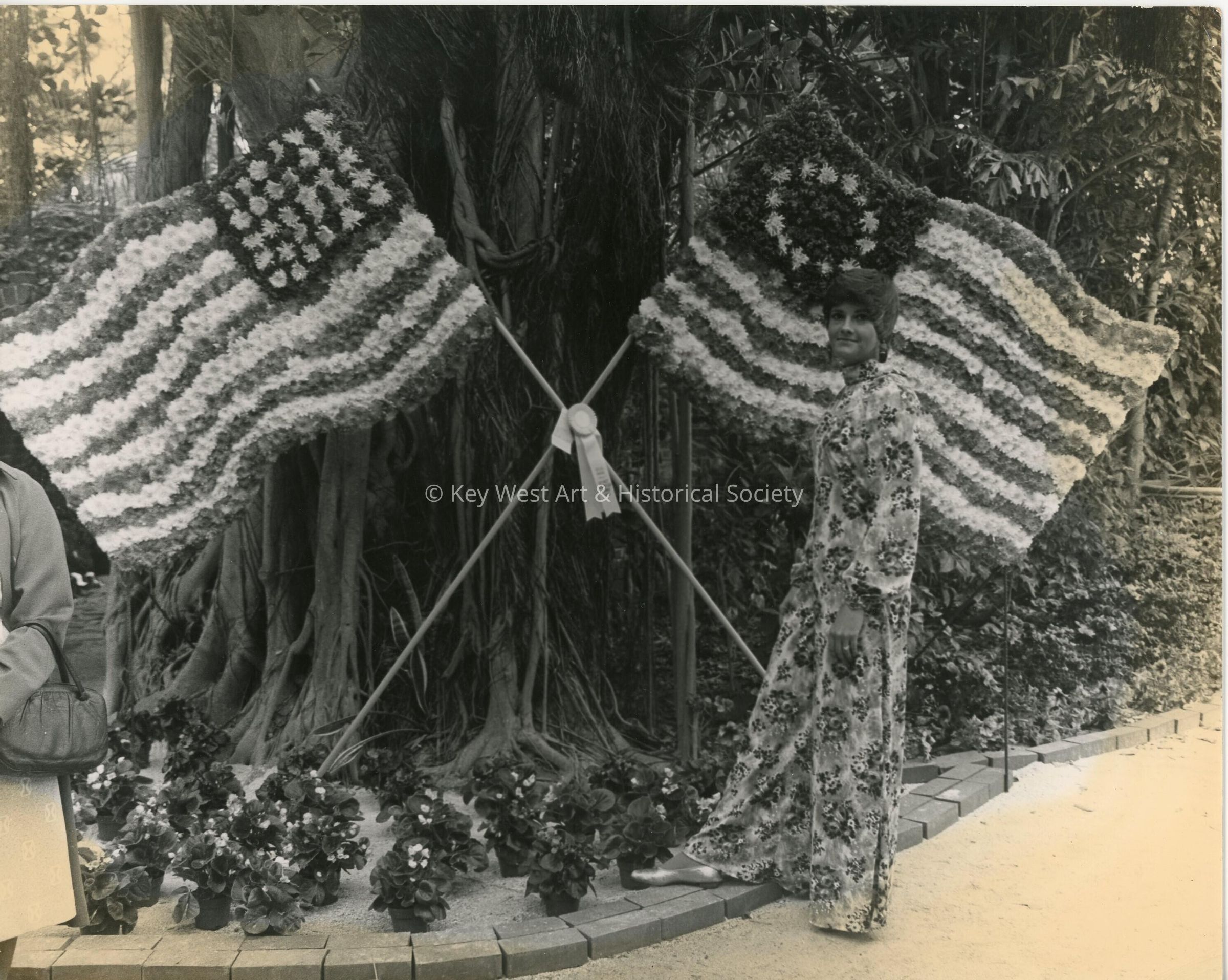 An unknown woman standing next to a tree and 2 flags