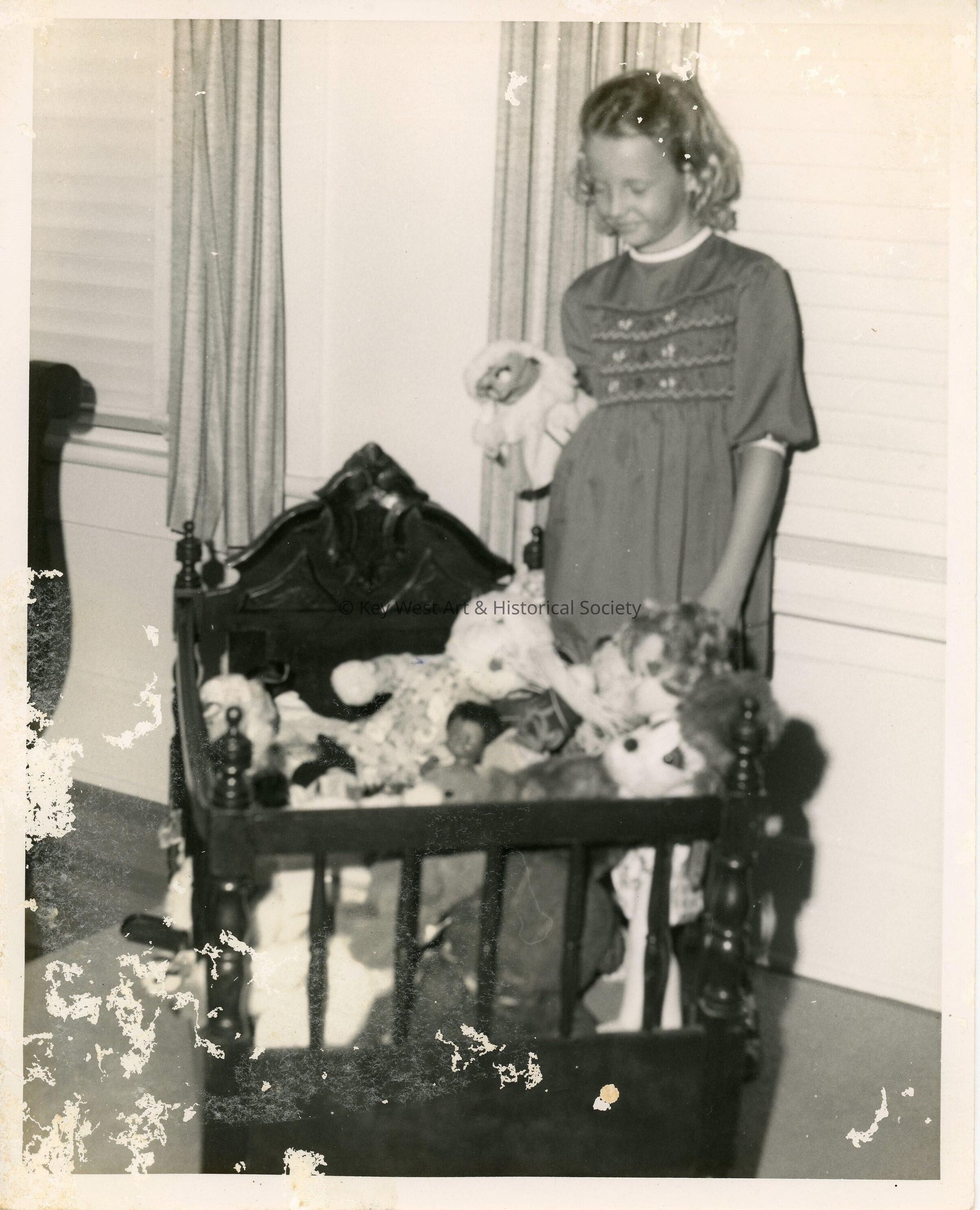 An unknown child looking down at stuffed animals in a cradle
