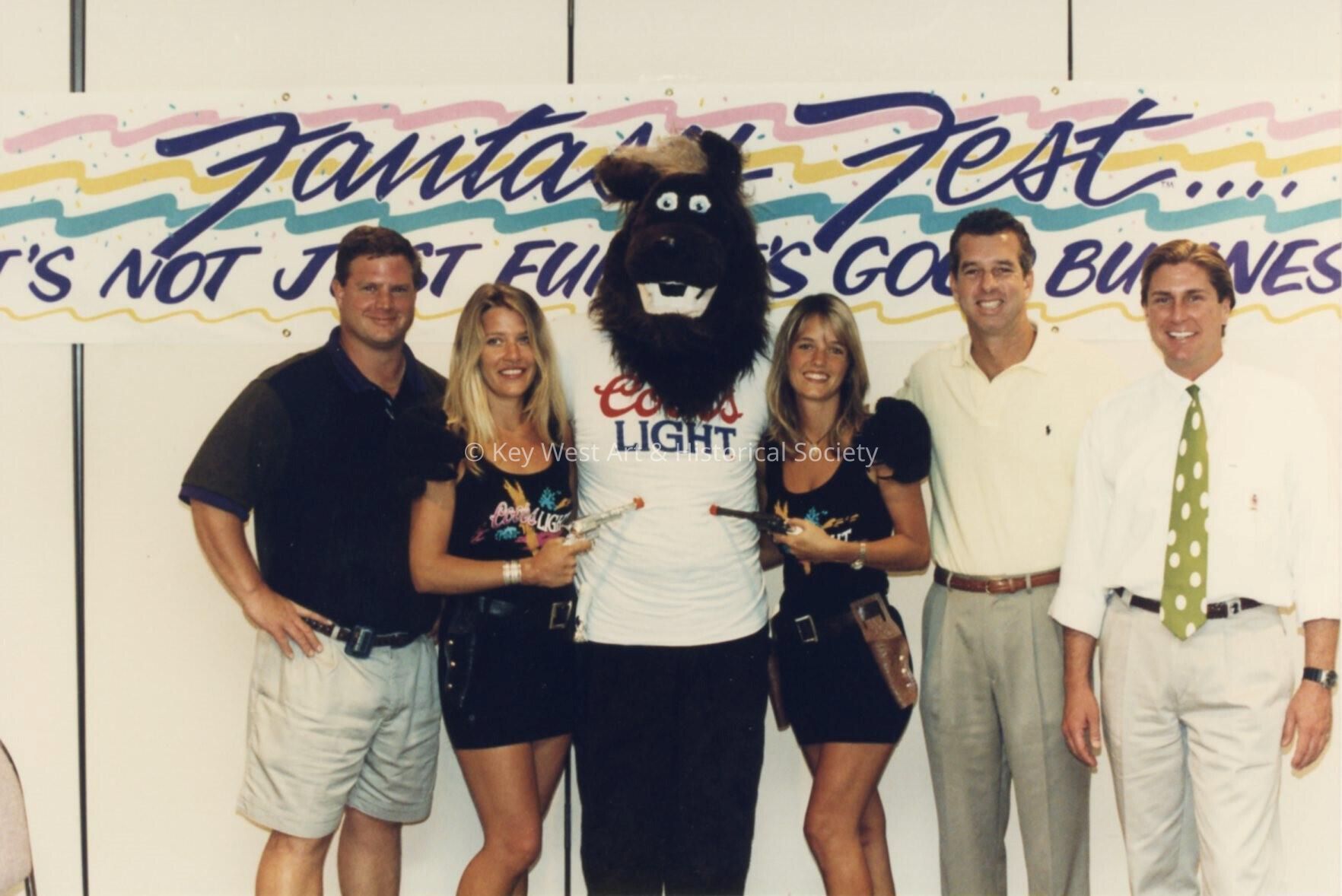 A group of unknown people standing in front of a Fantasy Fest sign.