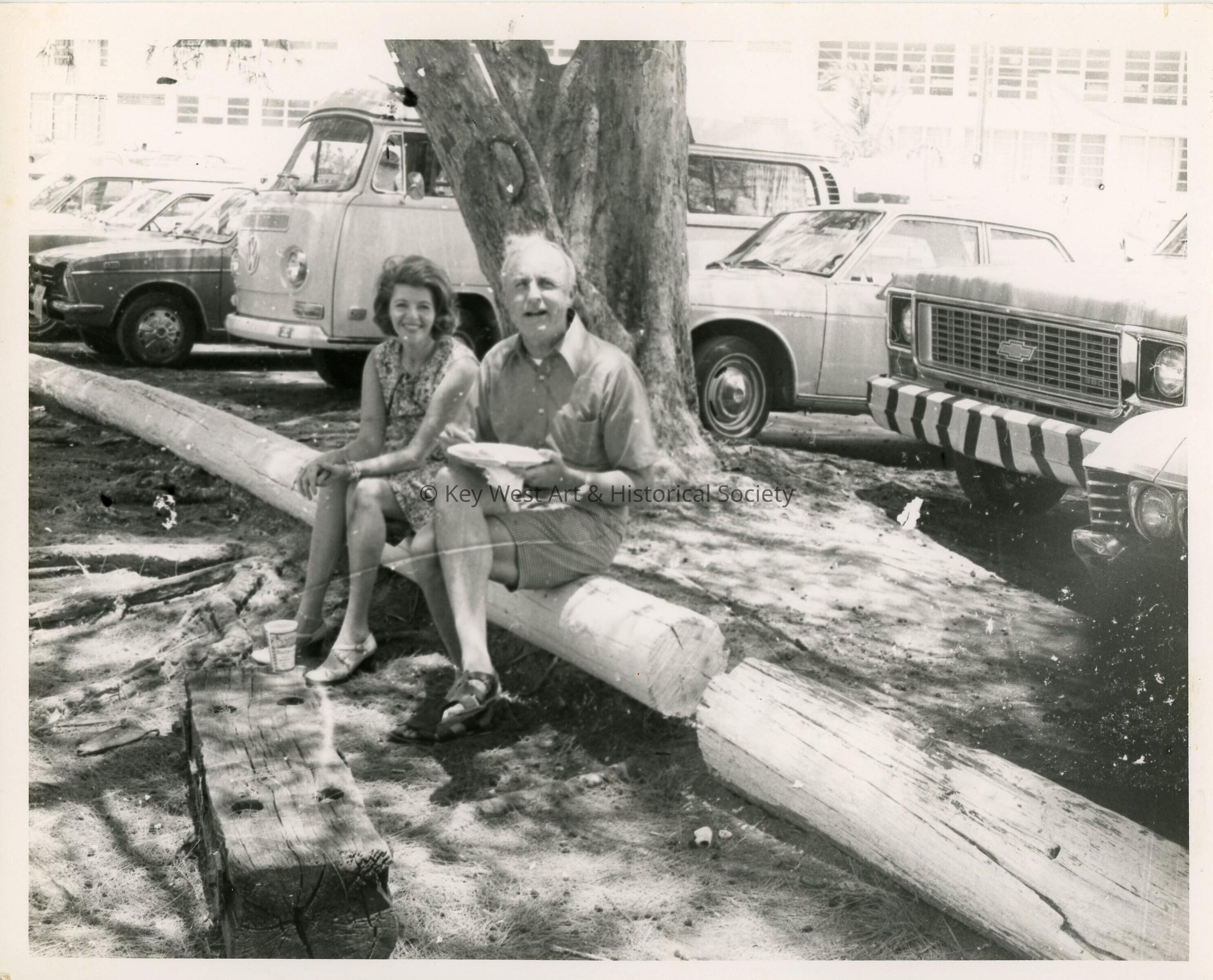 An unknown male and female eating while sitting on a log