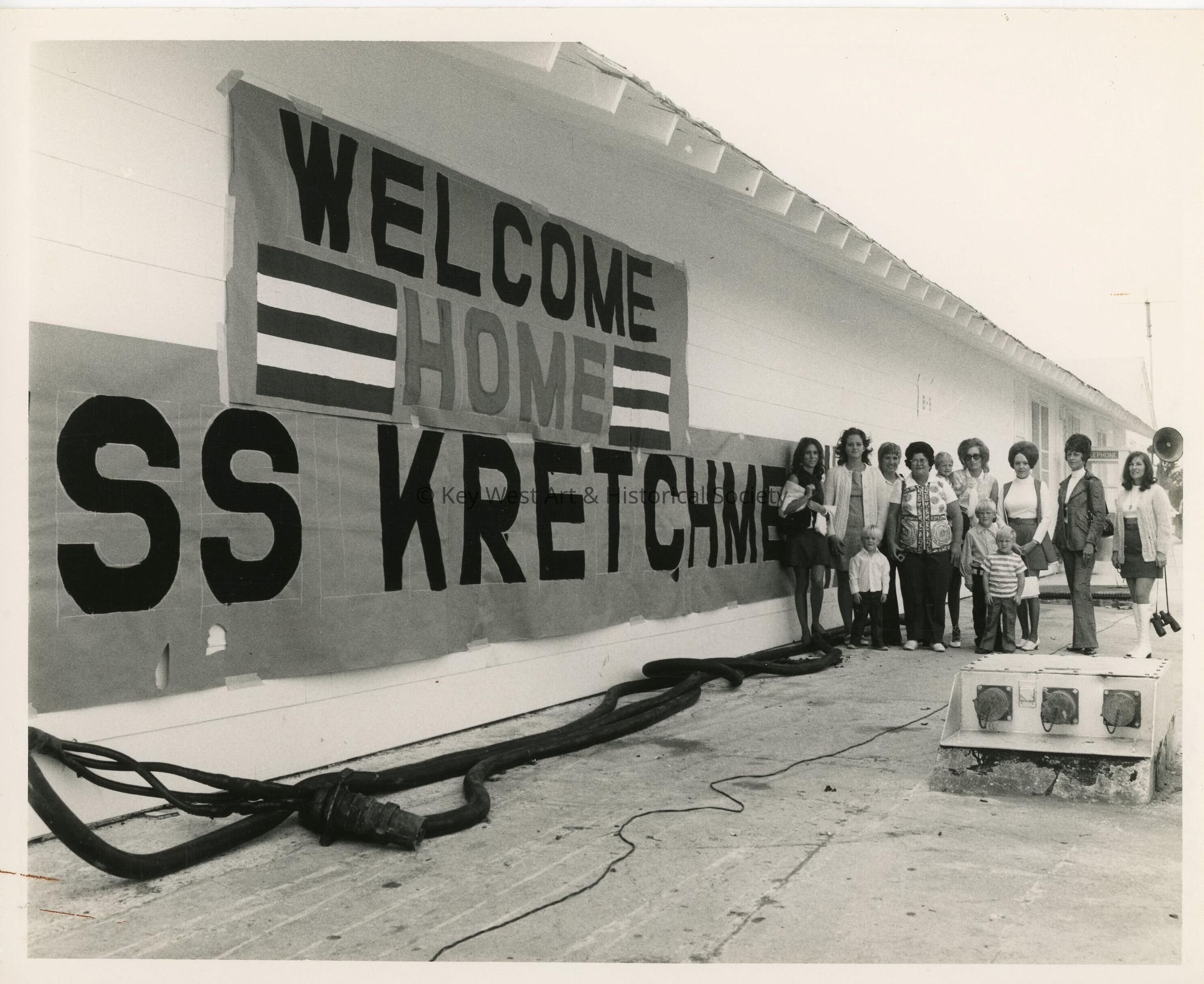A group of unknown people standing next to a welcome home sign