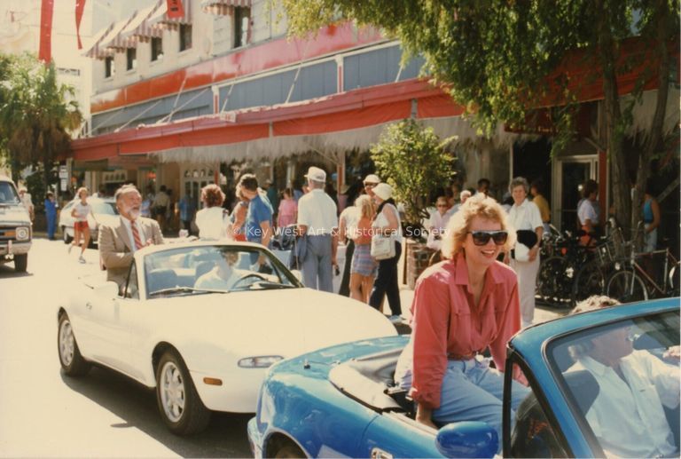 2 unknown people sitting on the top of a convertible going down Duval Stree