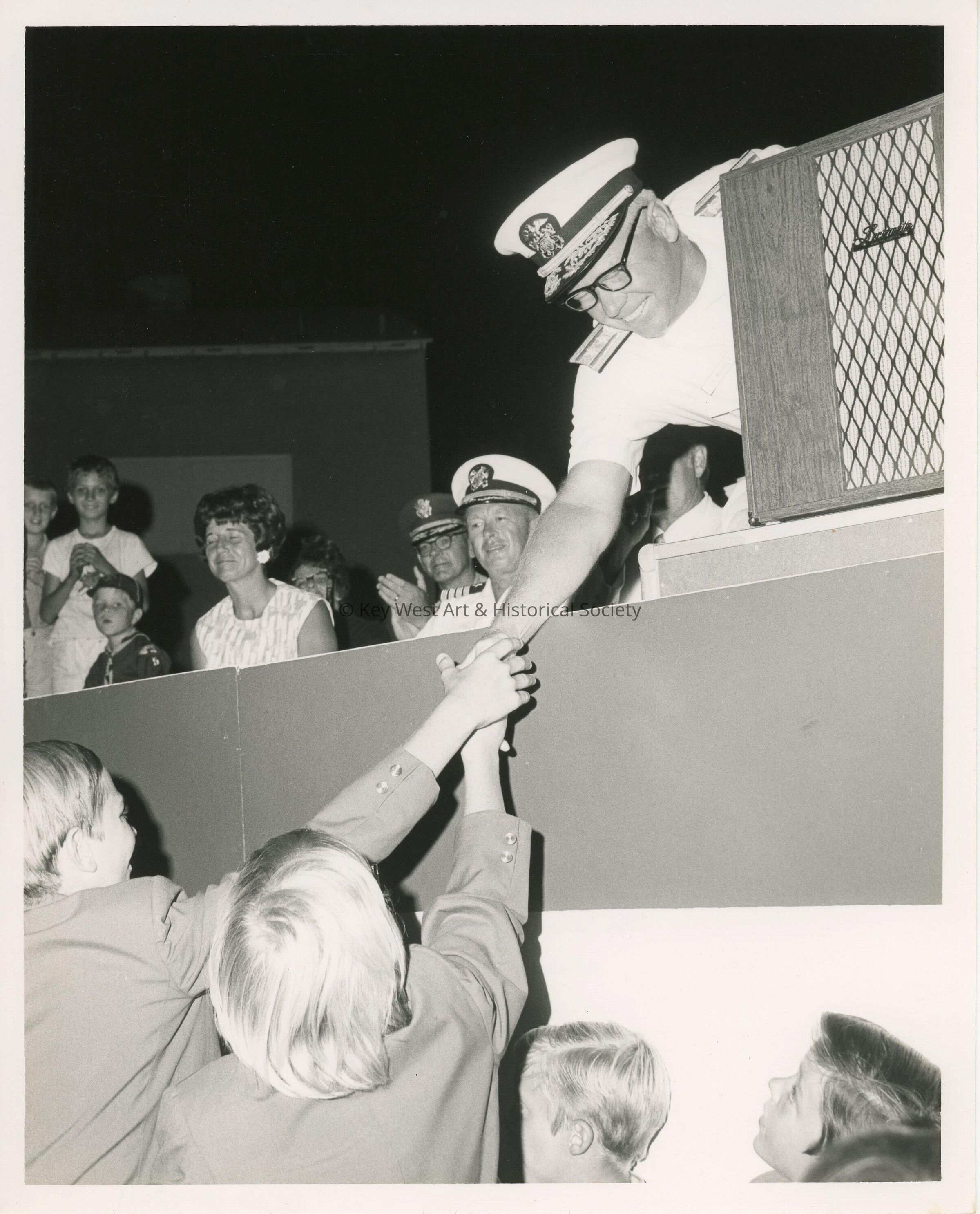 An unknown man at a podium leaning over and shaking hands