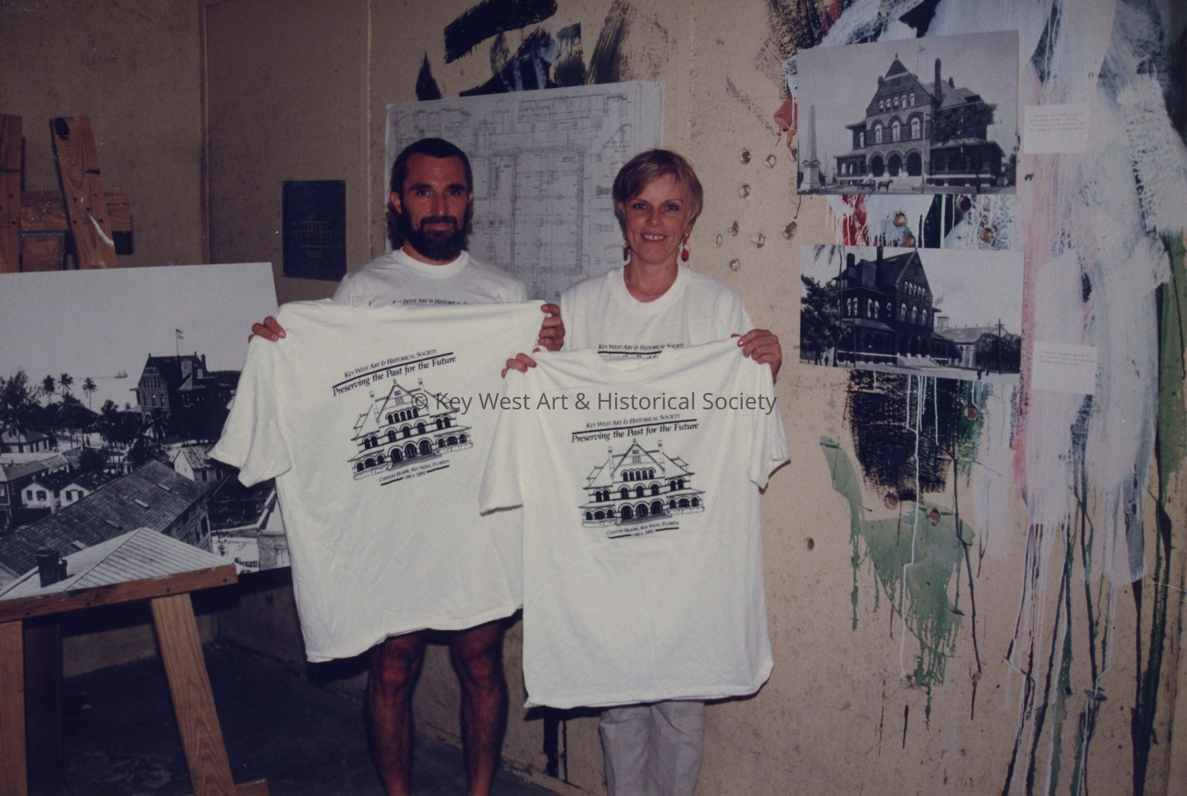 An unknown man and woman holding up t-shirts that have the Custom House on