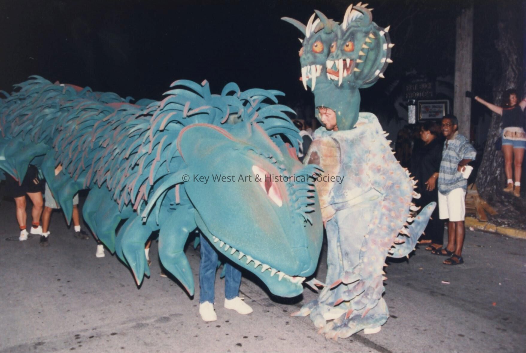 A dragon in  the parade being moved down the street with unknown people und