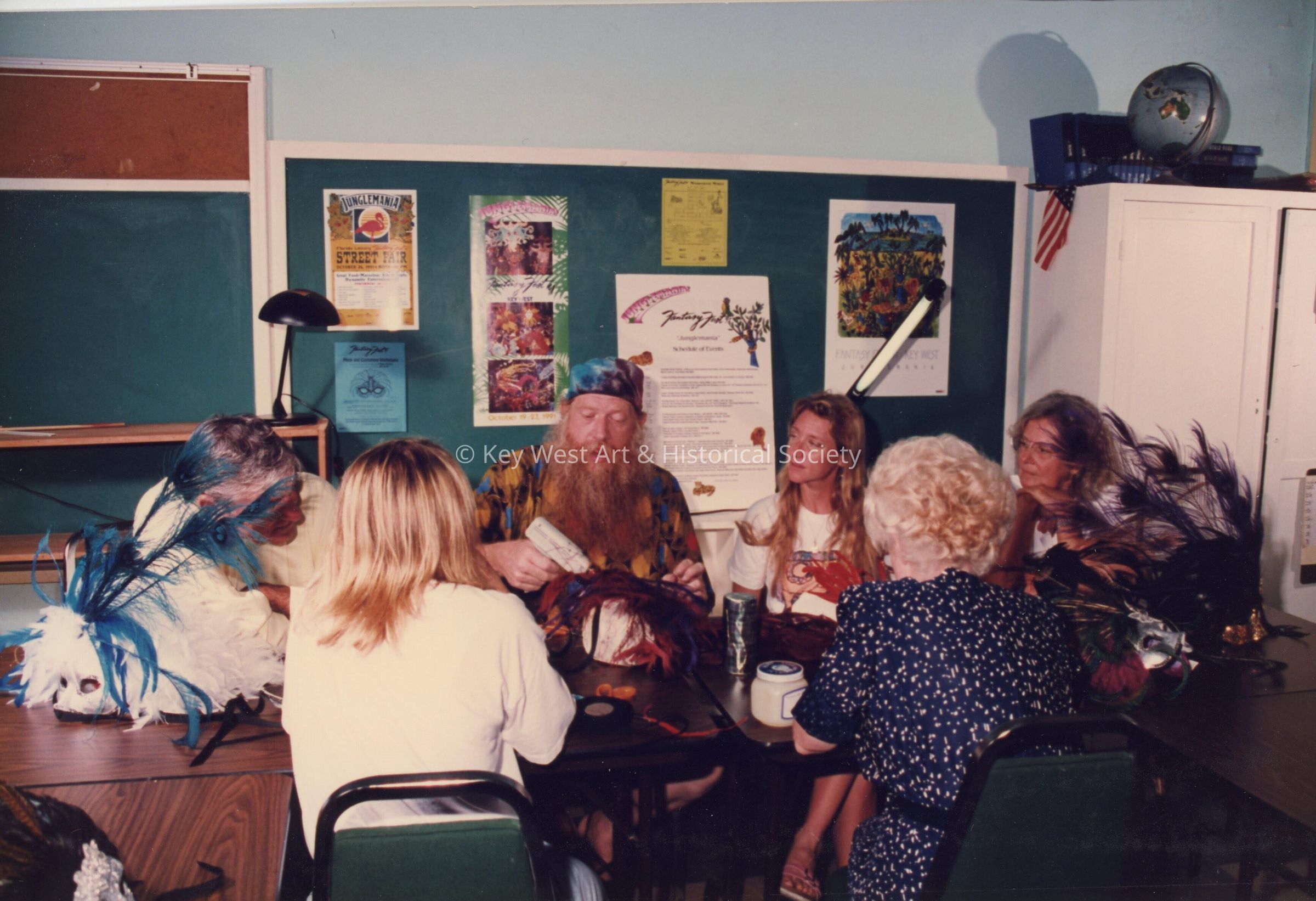 A group of unknown people sitting at a table making face mask.