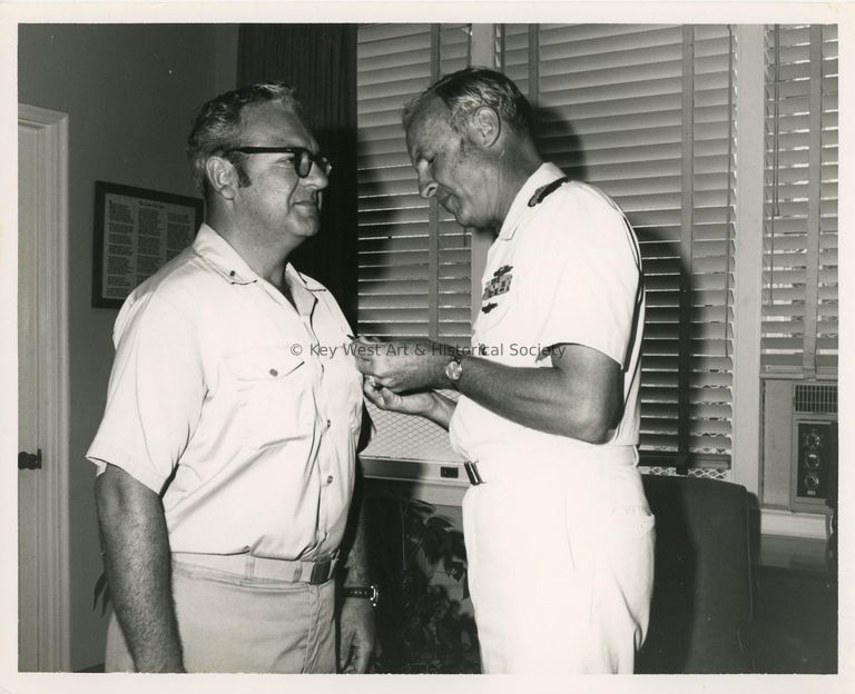 2 Unknown men in uniform, one is putting a pin on the others shirt