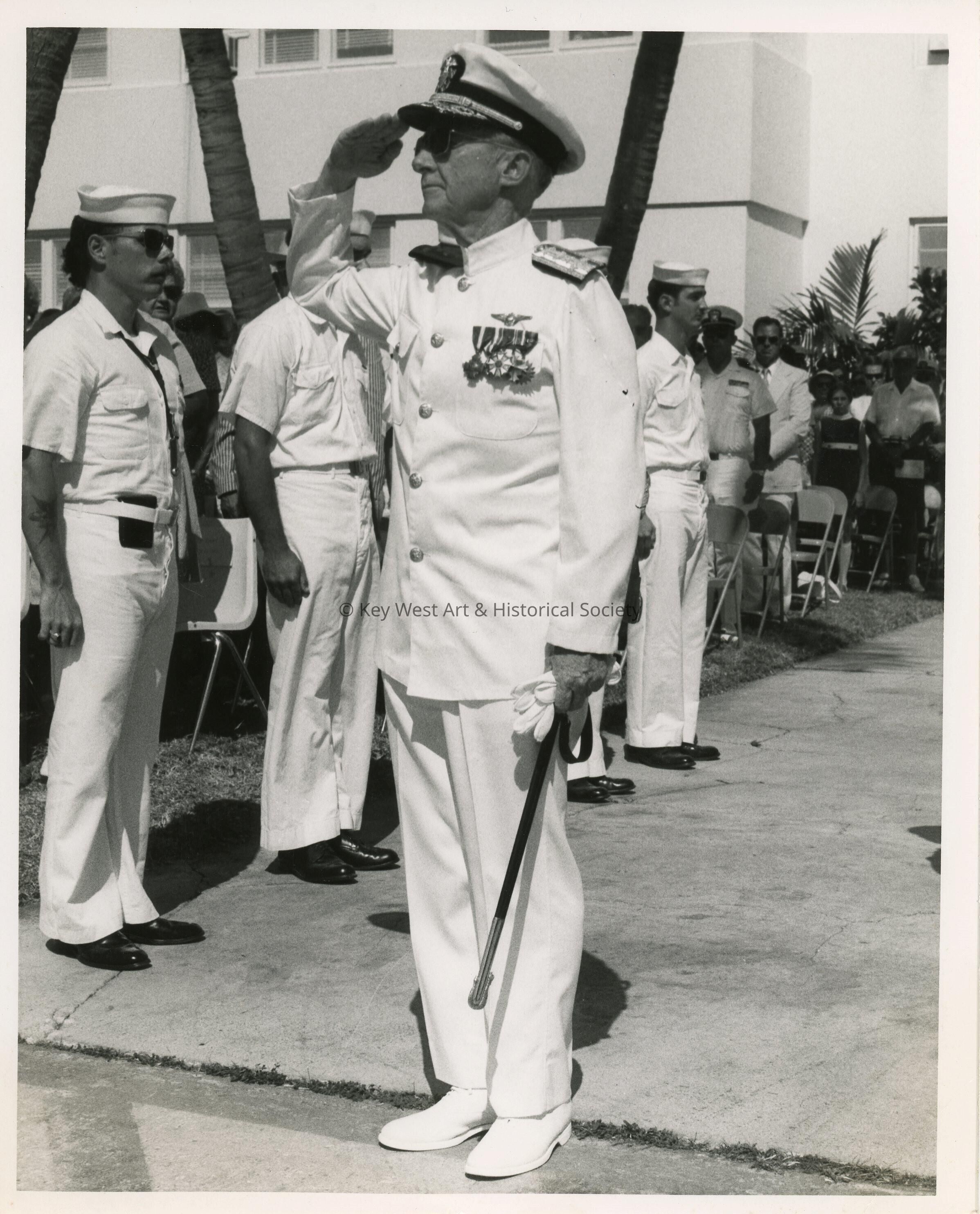 An unknown man in uniform standing at attention with others standing around