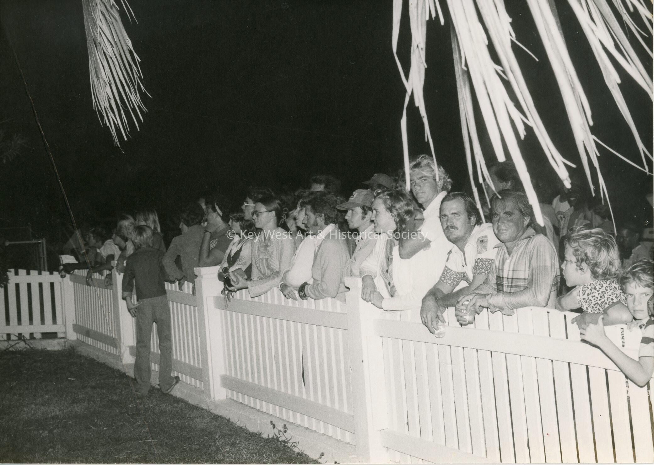 A group of people standing against a fence