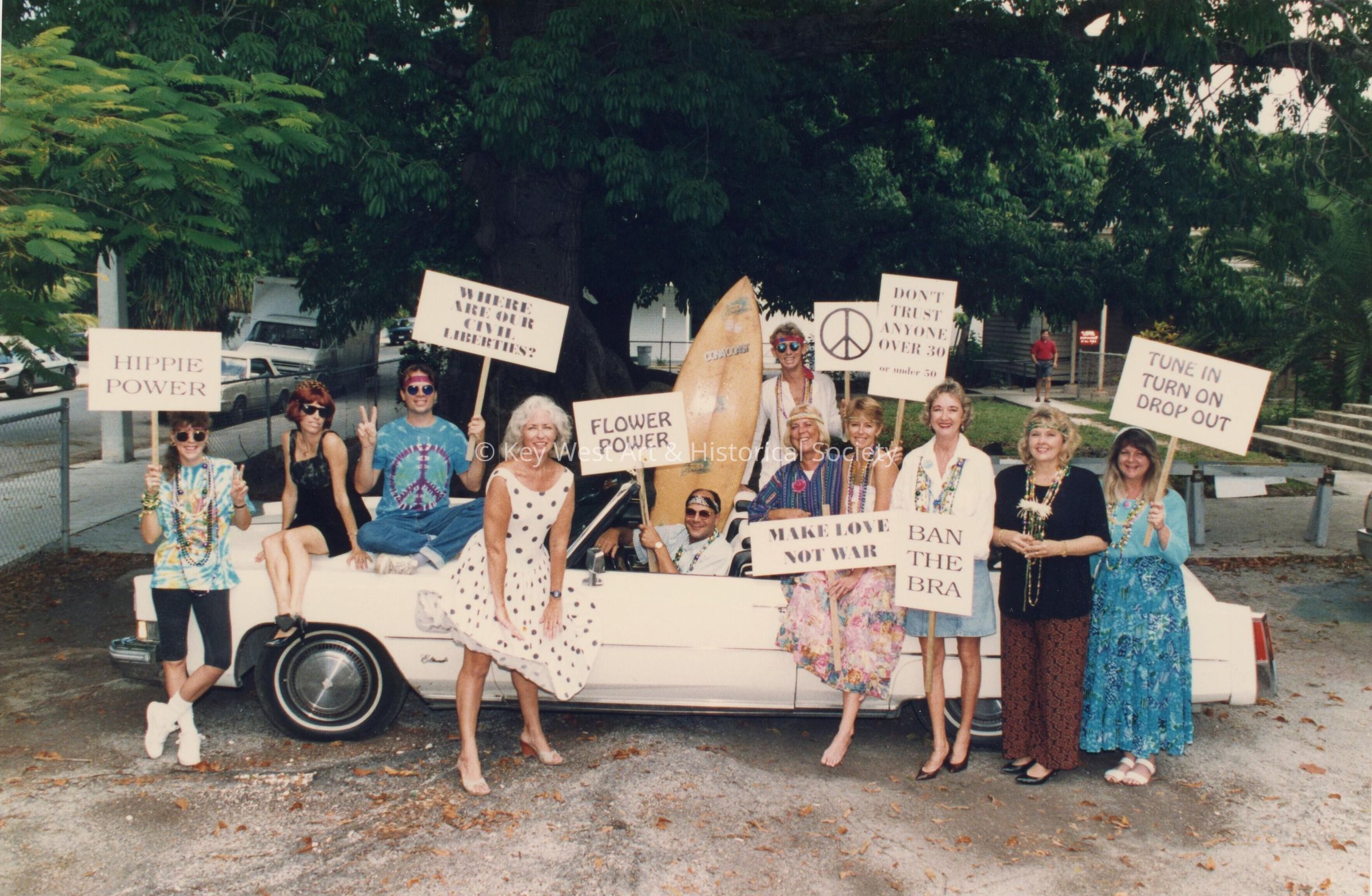 A white convertible with a group of unknown people some are standing near t