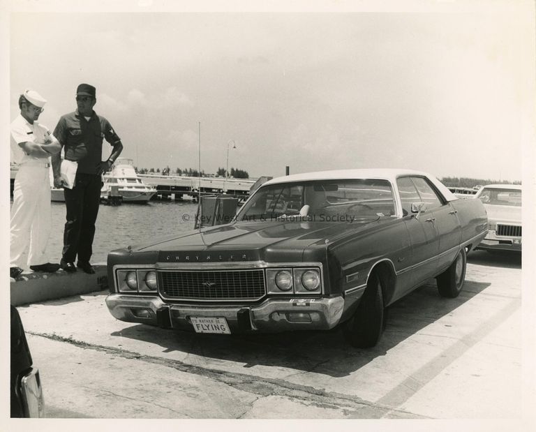 2 Unknown men in uniform standing on a pier next to an old car