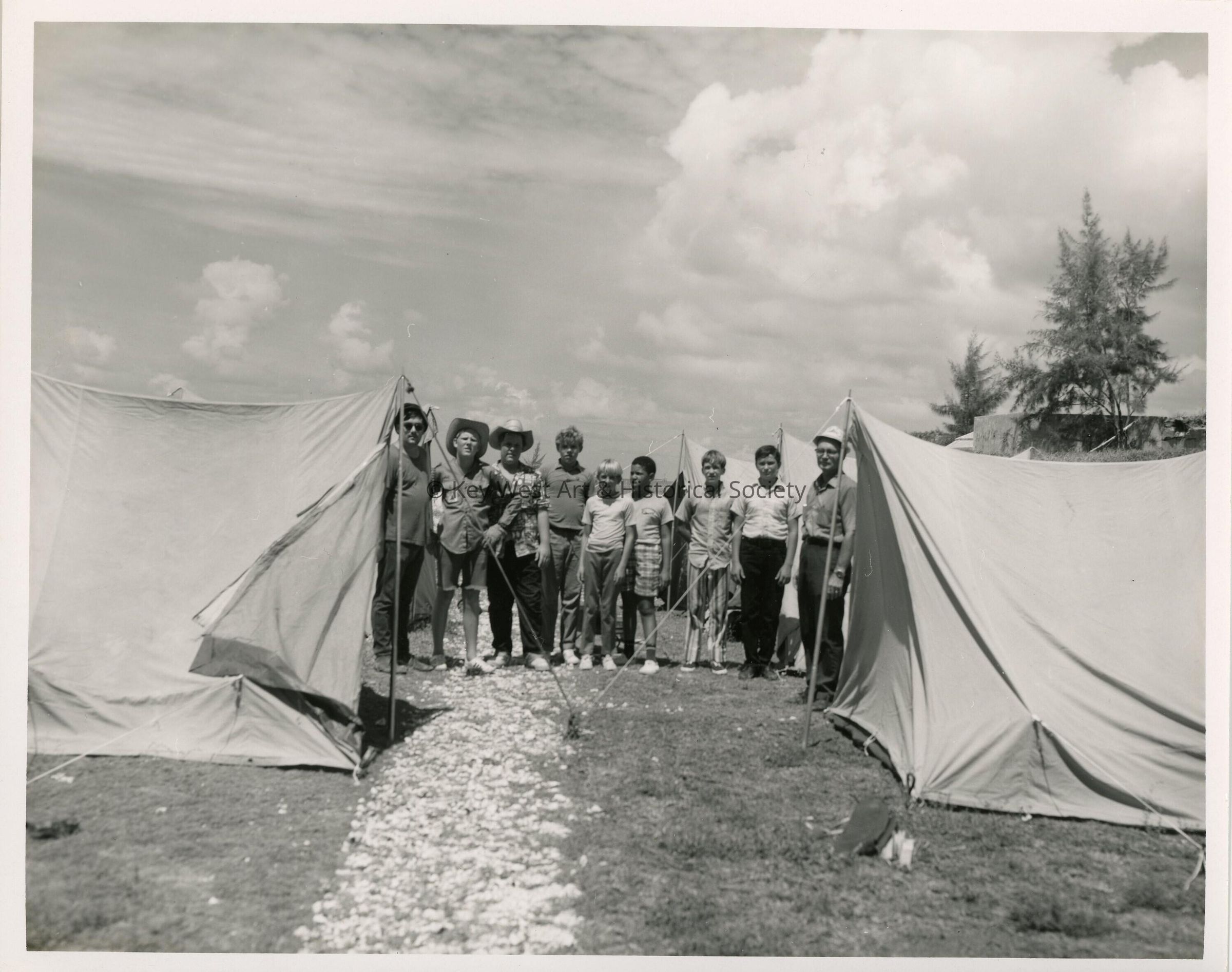 A group of unknown men and children standing next to tents