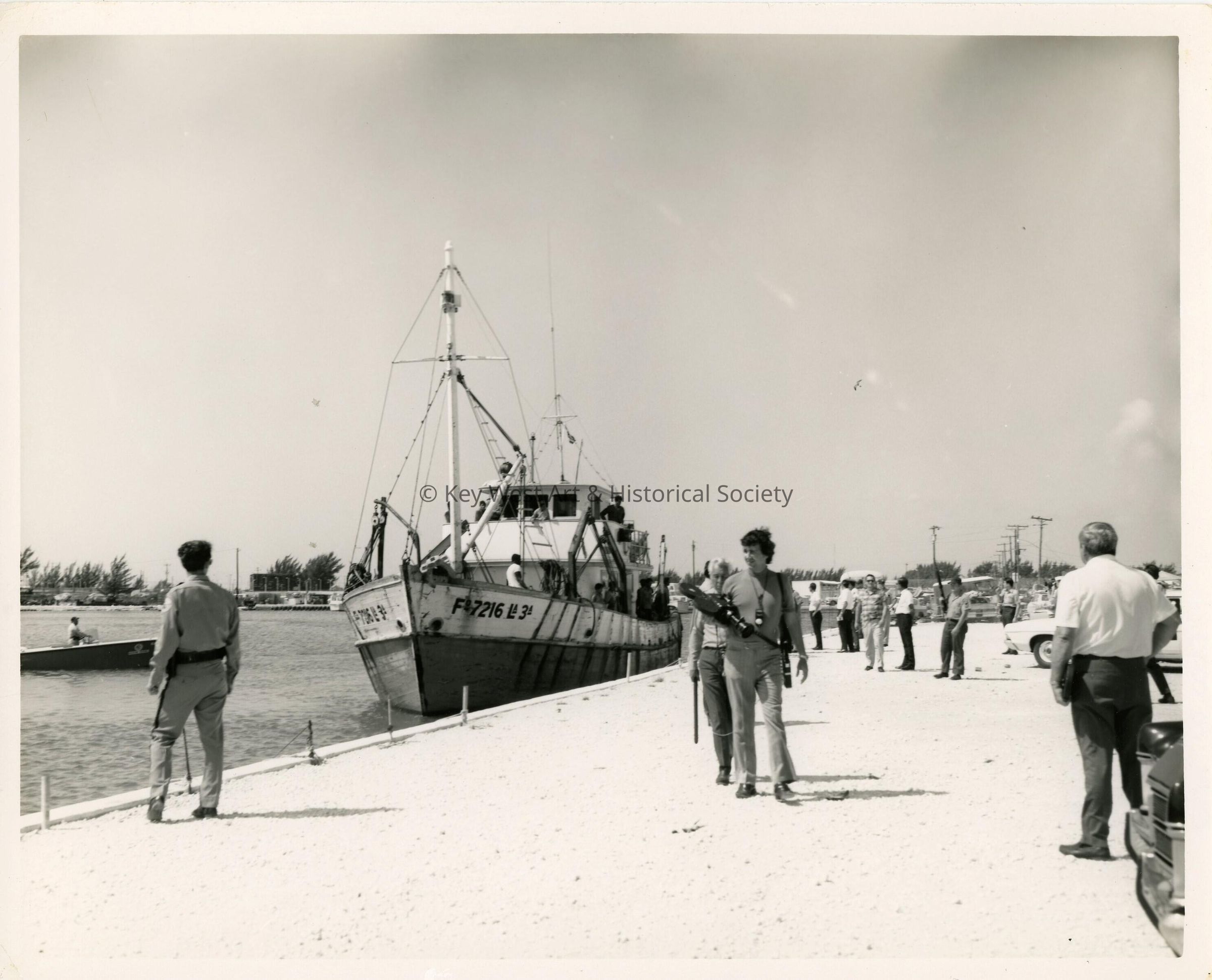 A group of unknown people on a pier with a few boats