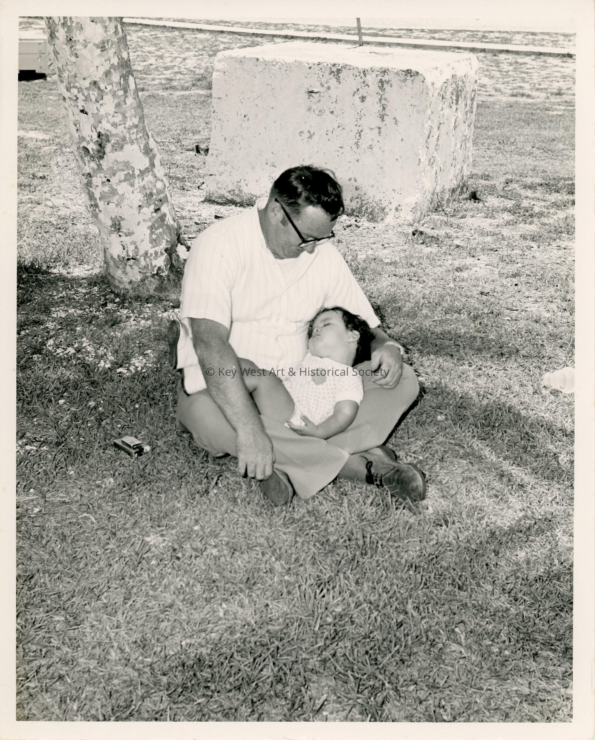 An unknown man holding a sleeping baby on the lawn