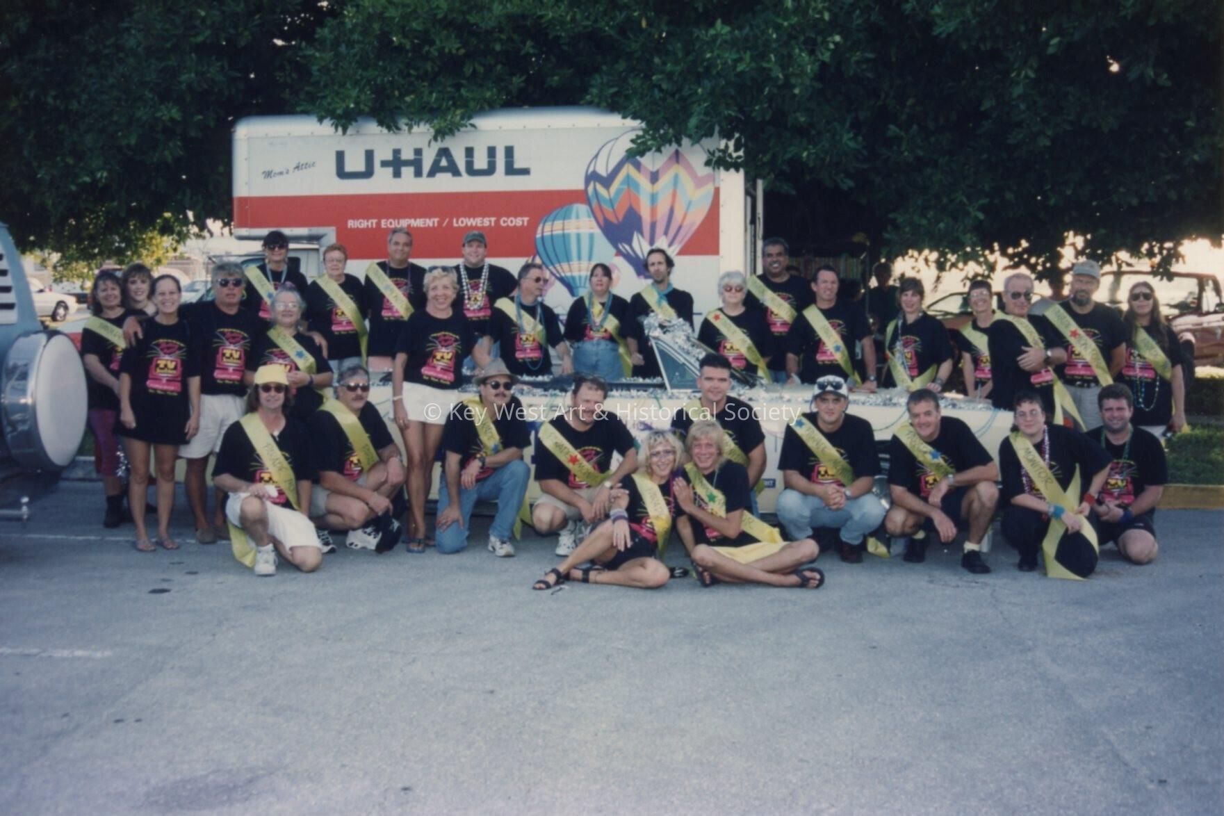A group of unknown people in front of a car, they all have the same shirts