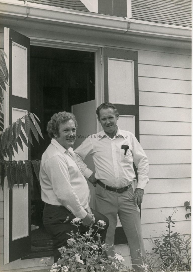 2 Unknown men standing outside next to a house/office