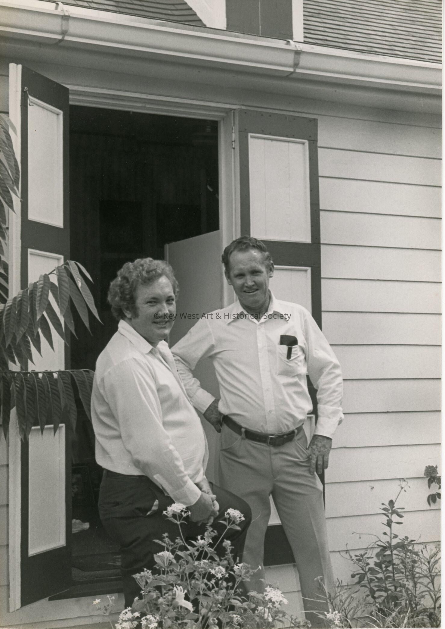 2 Unknown men standing outside next to a house/office