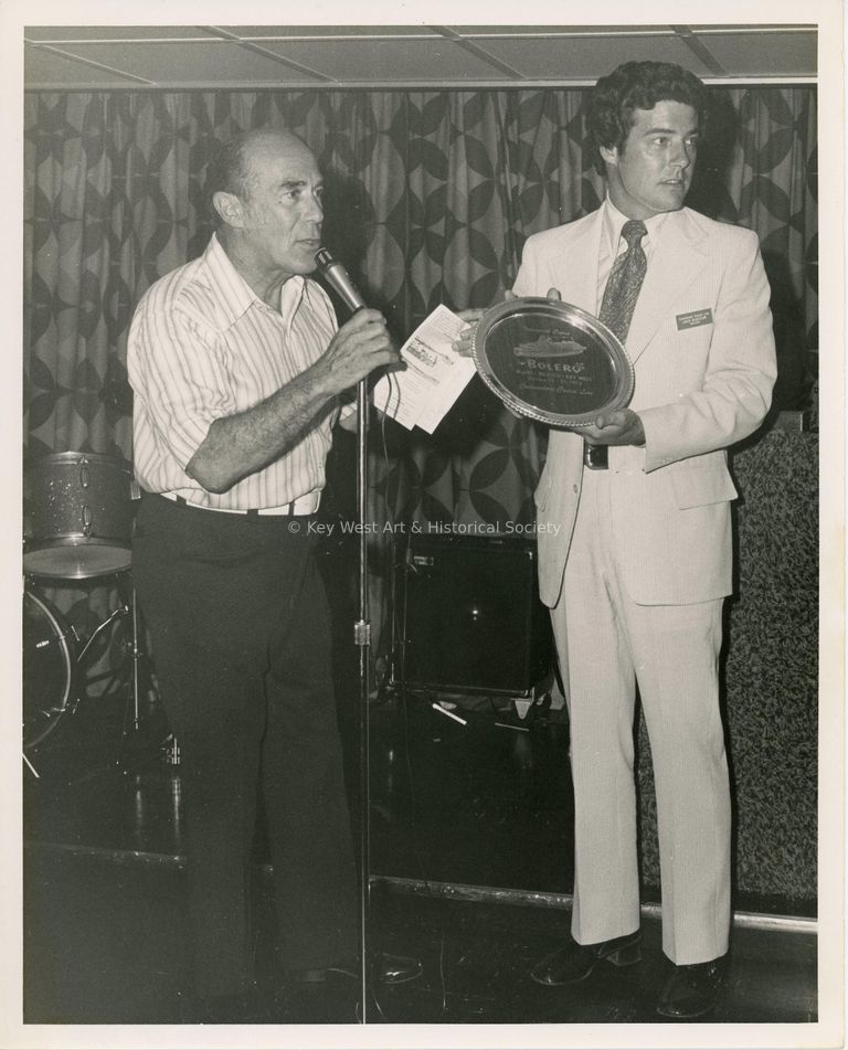 2 Unknown men standing at a microphone, one holding a plaque