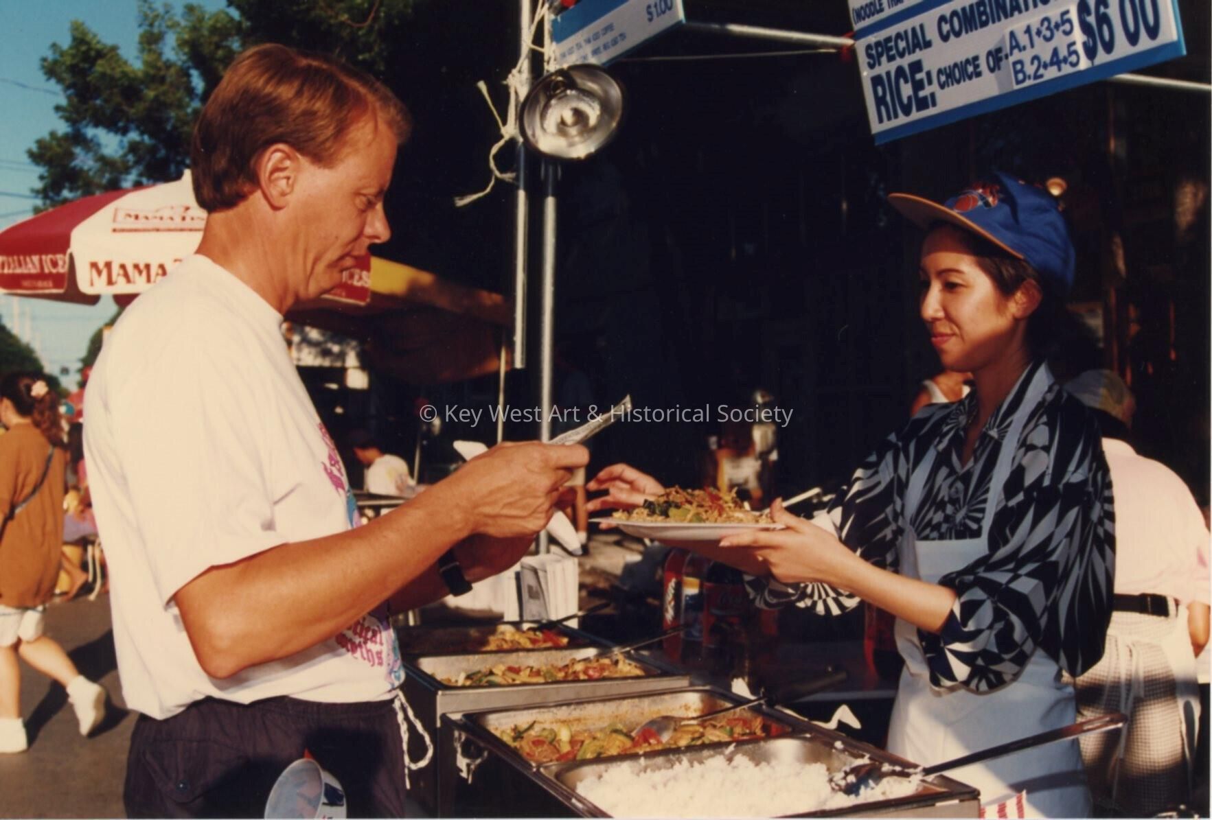 An unknown woman working a food booth, serving a plate of food to an unknow