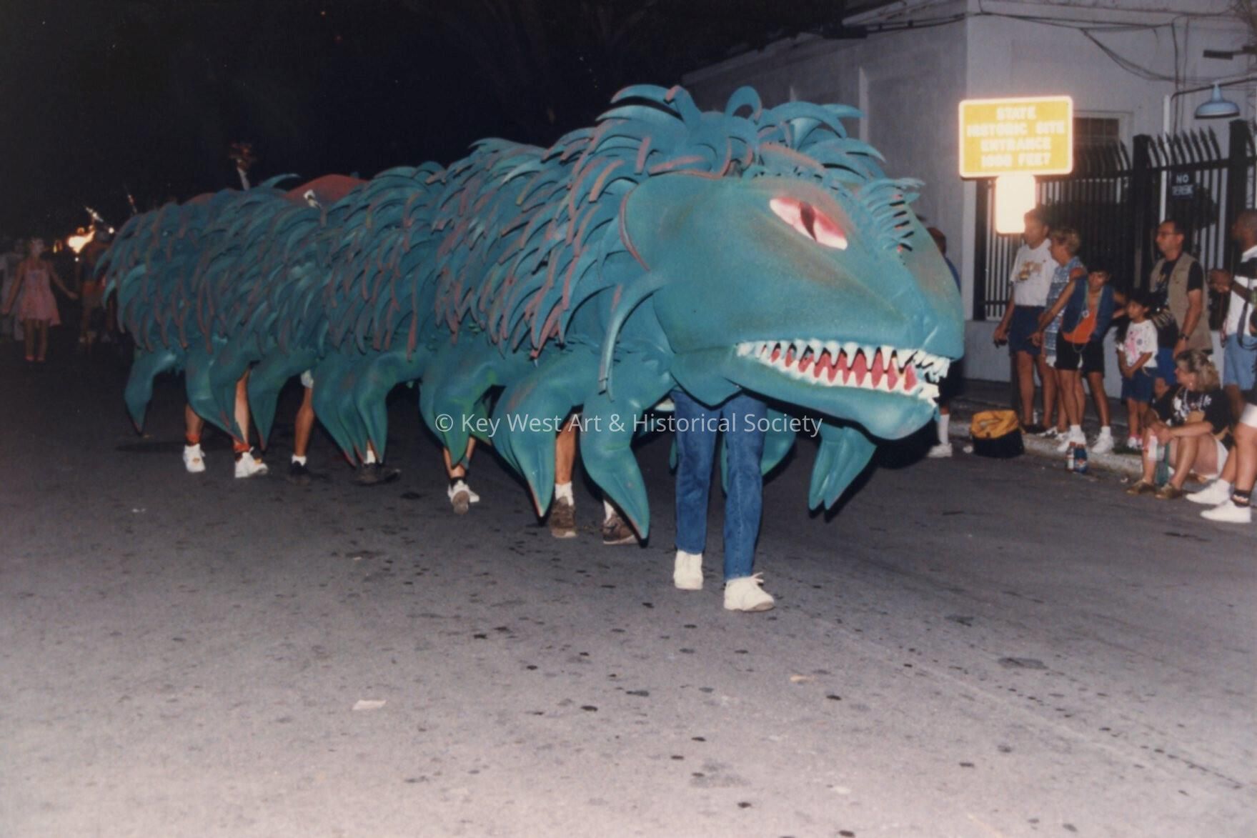 A dragon in  the parade being moved down the street with unknown people und