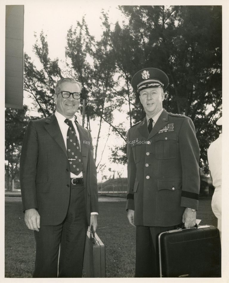 2 Unknown men standing  outside, one is uniform