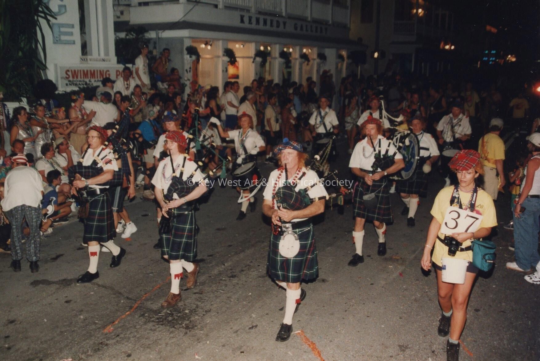 A pipe band playing while walking down the street in the parade.