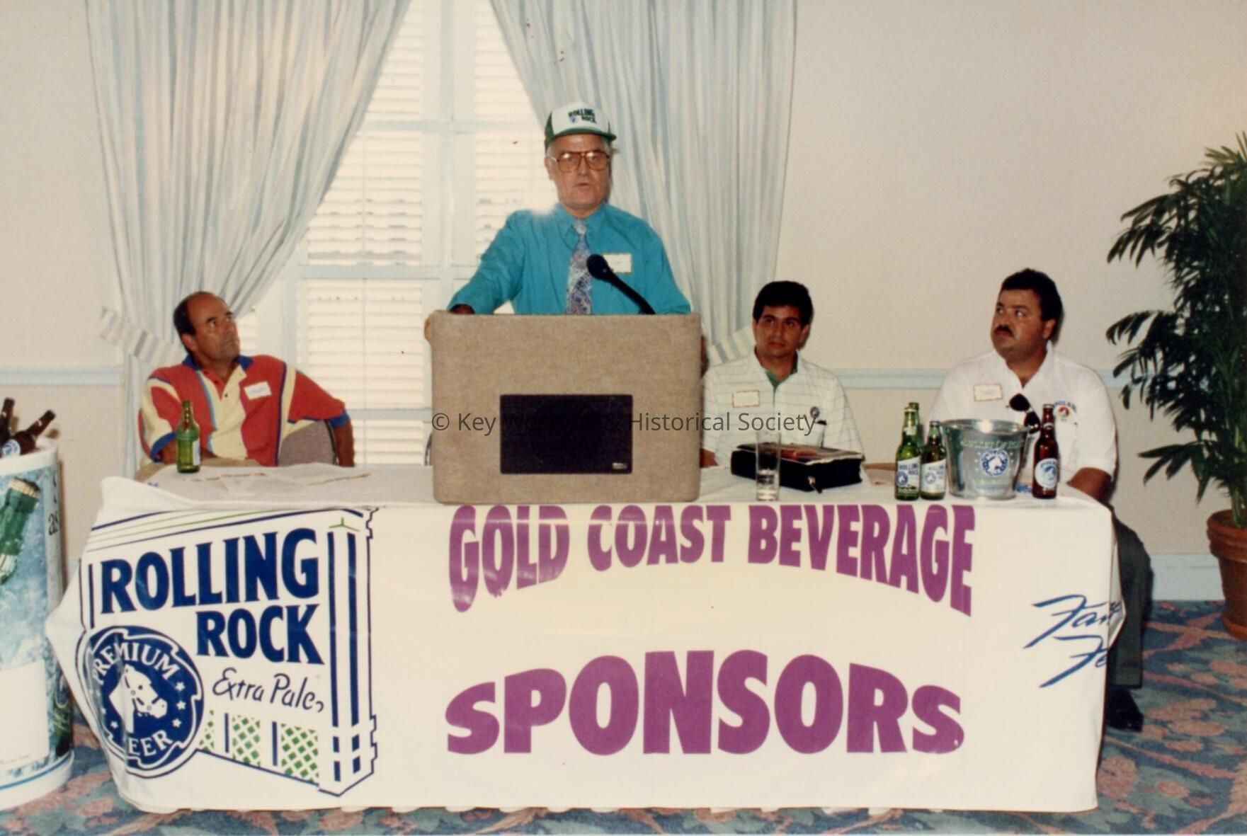 An unknown man speaking at the podium, a sign reads Gold Coast beverage spo
